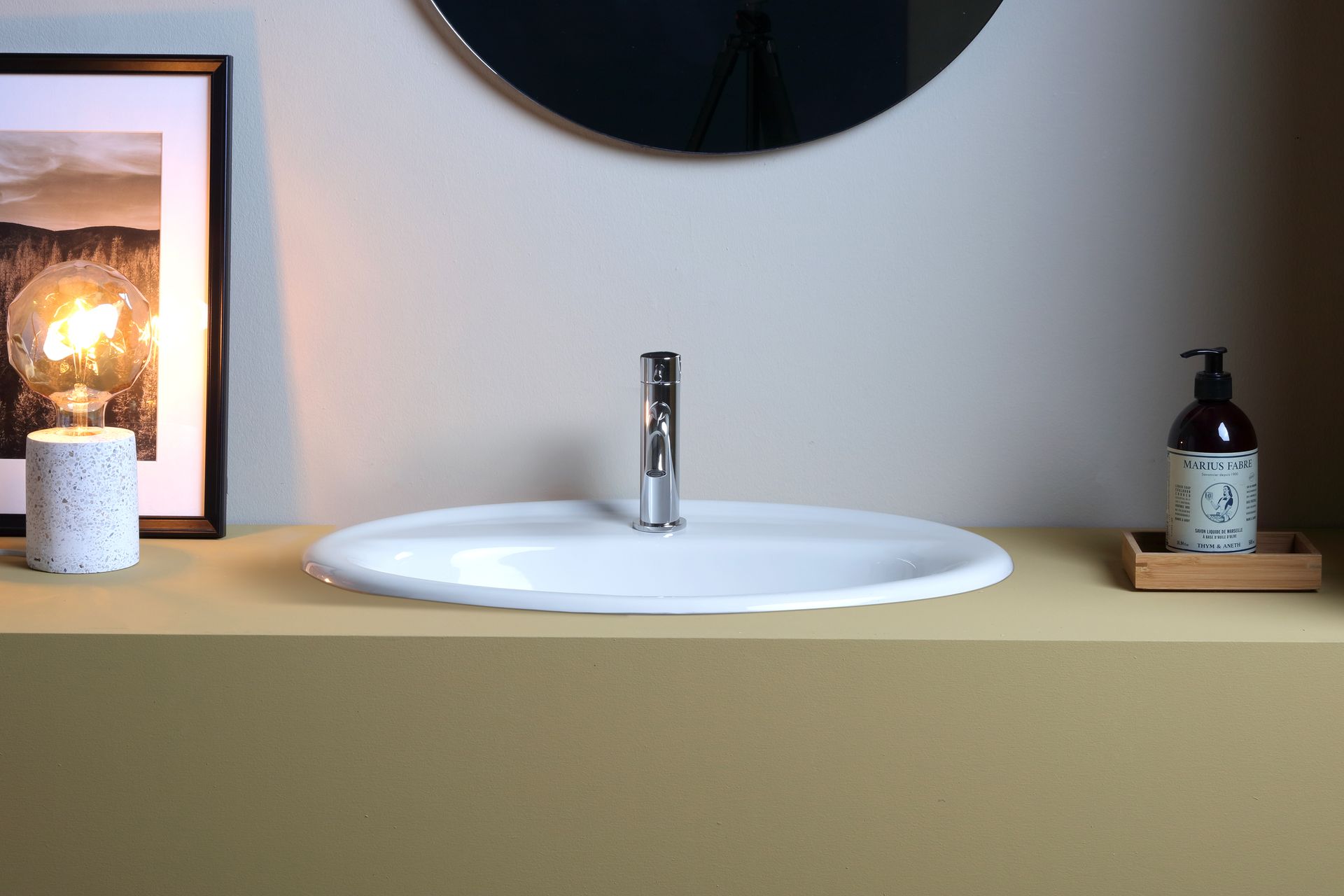 Lavandino bianco con rubinetto cromato su un bancone color cuoio, sotto uno specchio e una parete, con arredamento minimal.