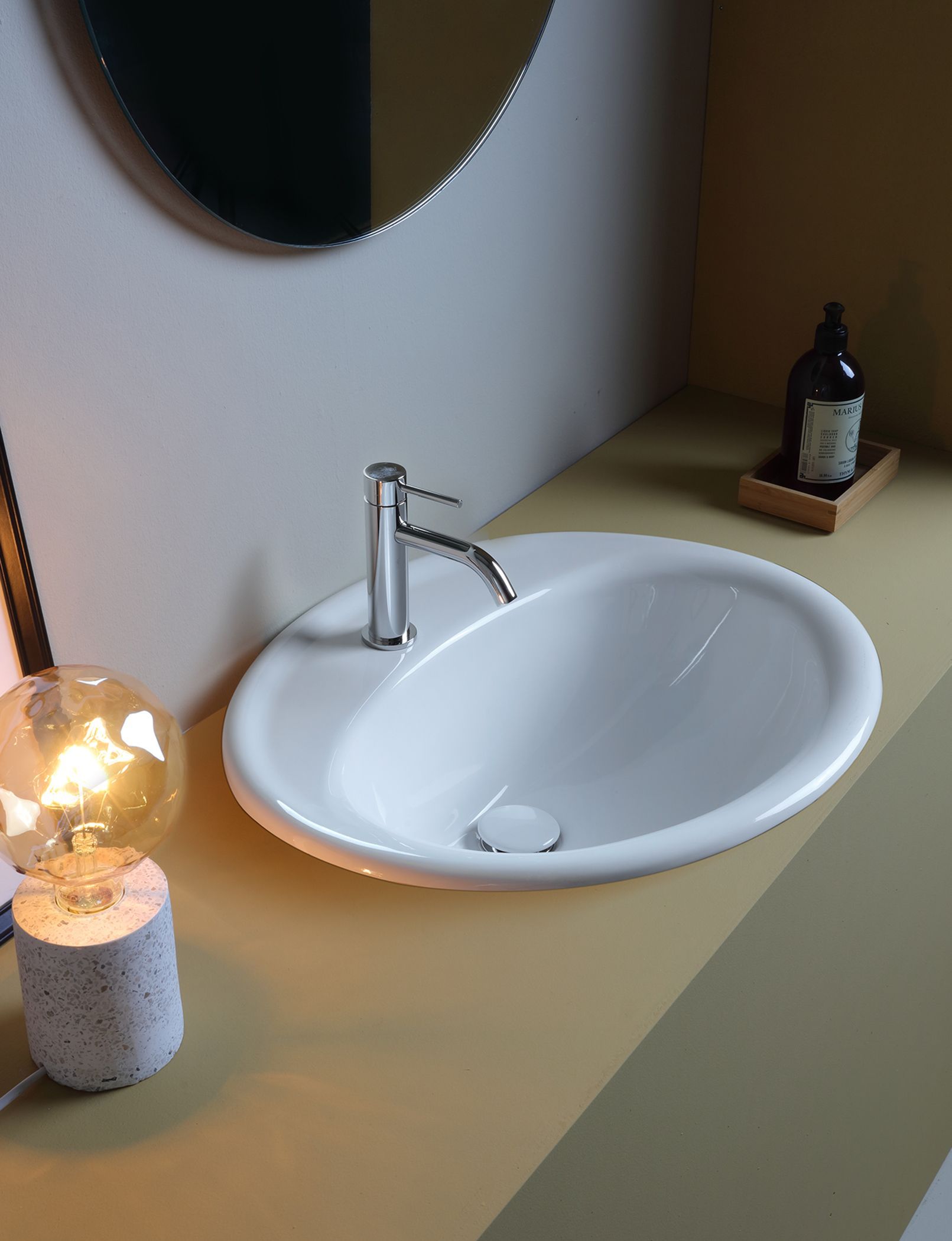 Lavandino ovale bianco con rubinetto cromato su un piano di lavoro giallo in un bagno.