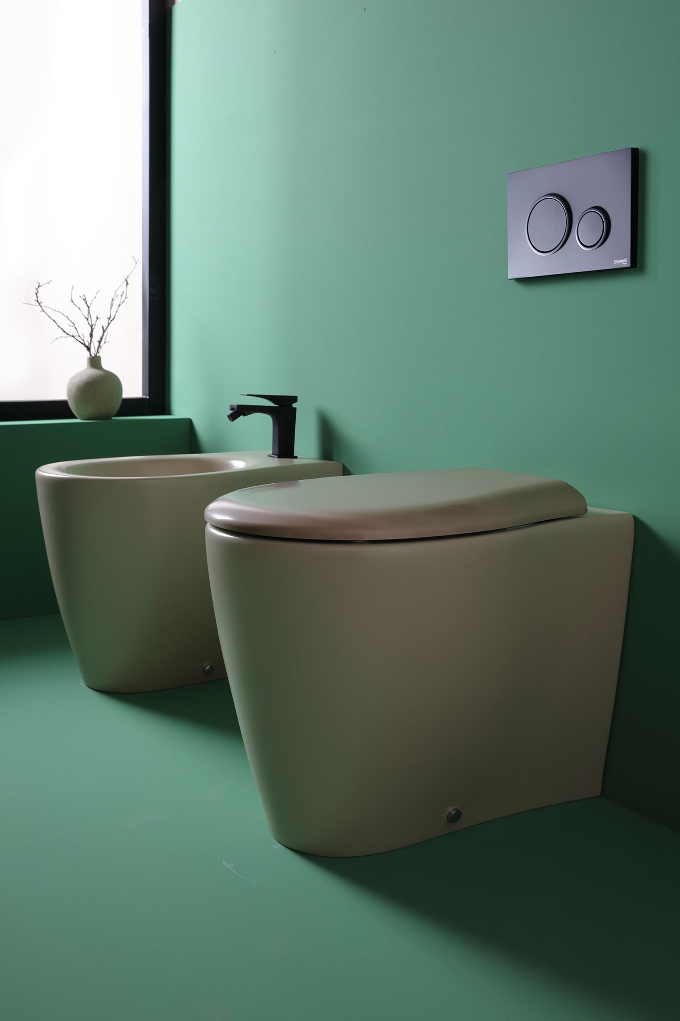 Un bagno moderno con WC e bidet, di fronte a una parete verde, con un rubinetto nero.