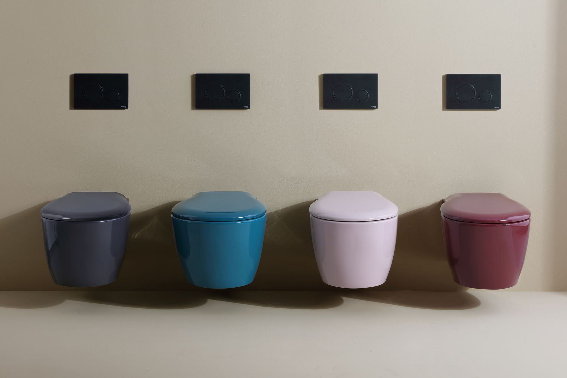 Quattro colorati WC sospesi nei toni del viola, blu, rosa e bordeaux, con pannelli di scarico sopra una parete beige.