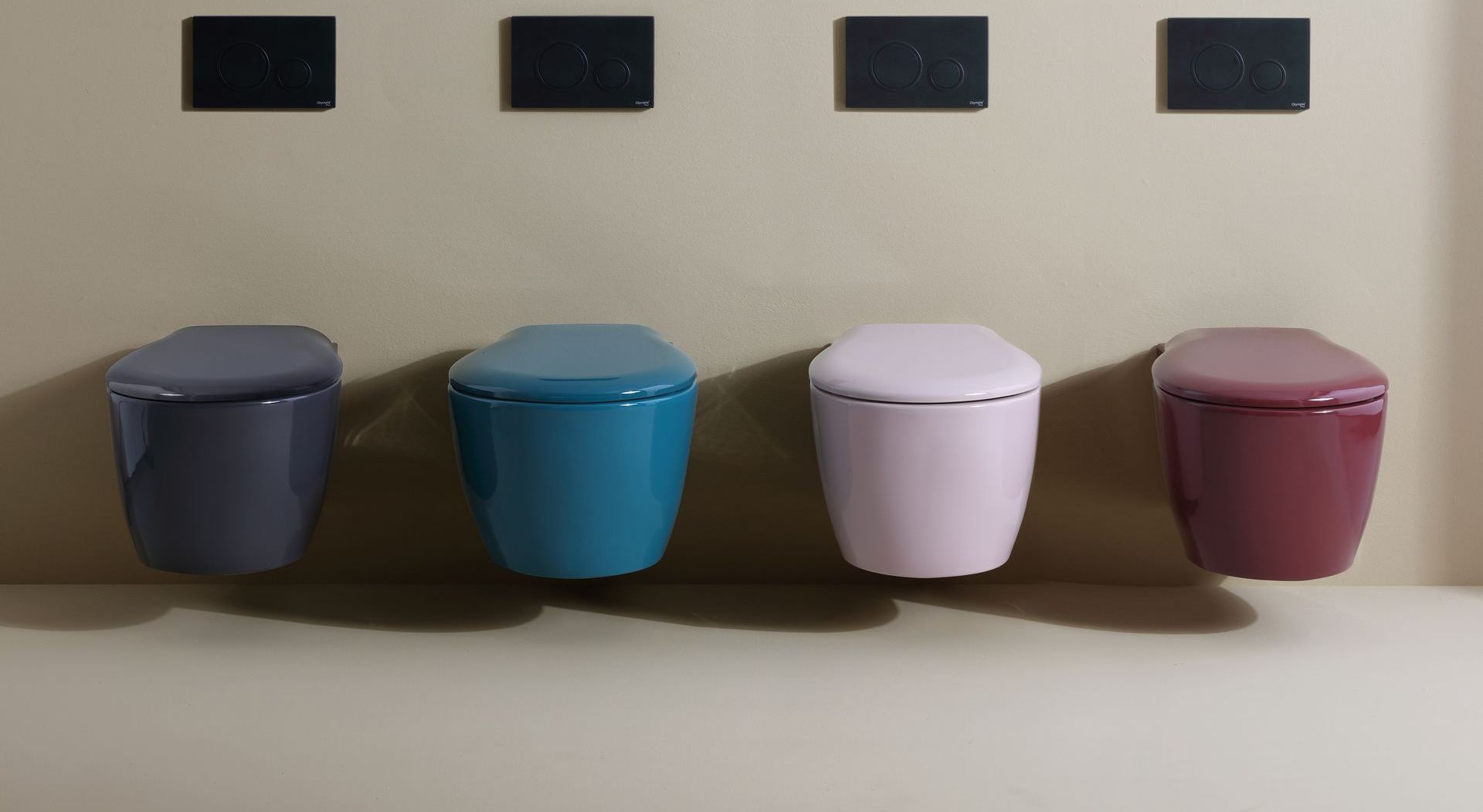 Quattro WC sospesi in vari colori (grigio, verde acqua, rosa, bordeaux) sotto insegne quadrate nere.