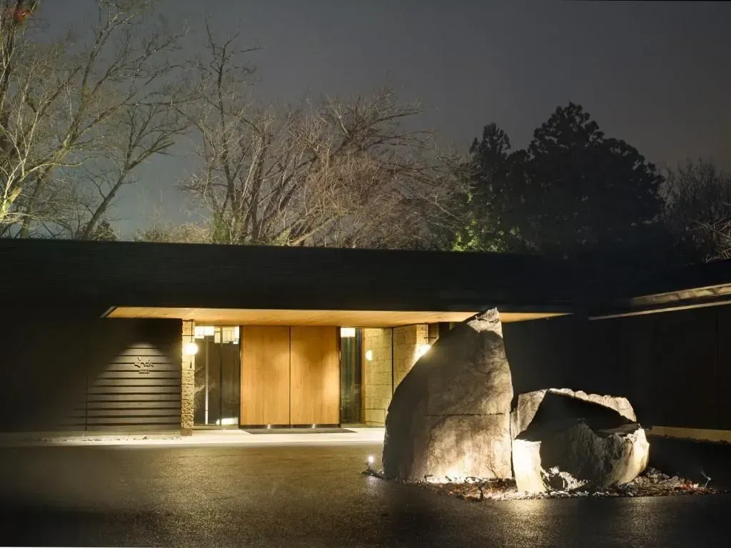 Vista notturna di un edificio moderno con porte in legno, illuminato da faretti con una grande formazione rocciosa di fronte
