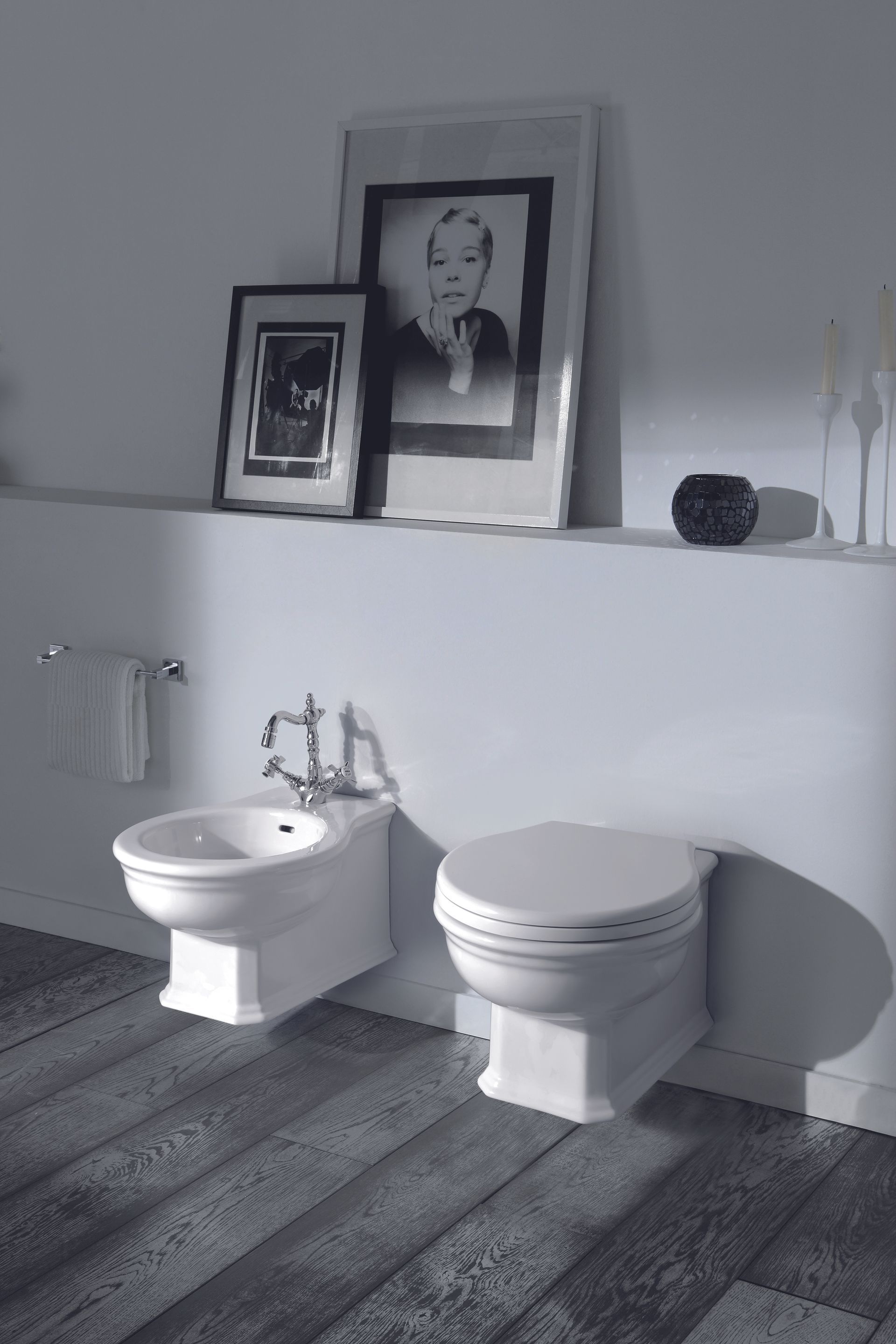 Bagno con WC e bidet, sotto una mensola con foto incorniciate e decorazioni.