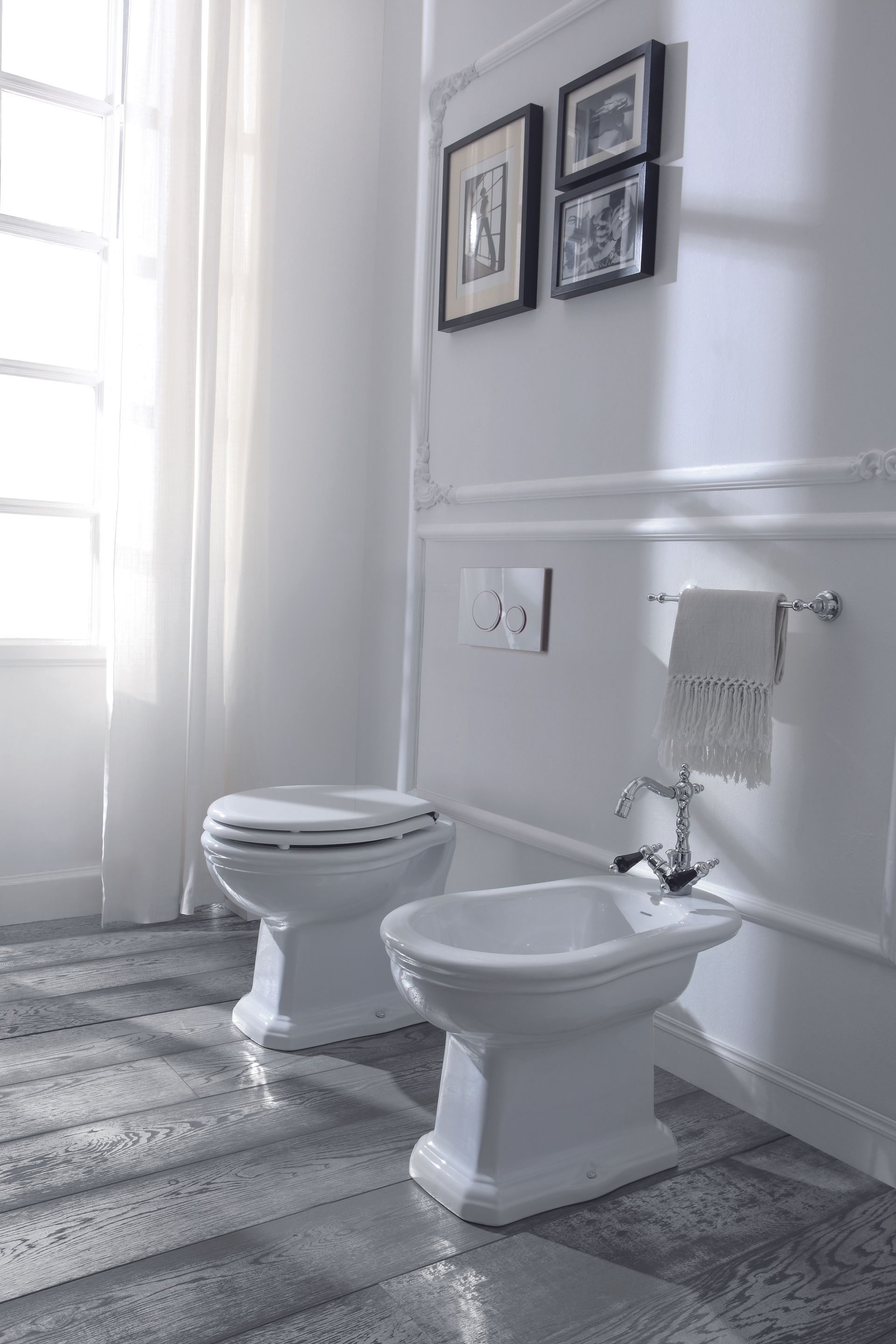 WC e bidet bianchi in un bagno con finestra e quadri incorniciati alla parete.