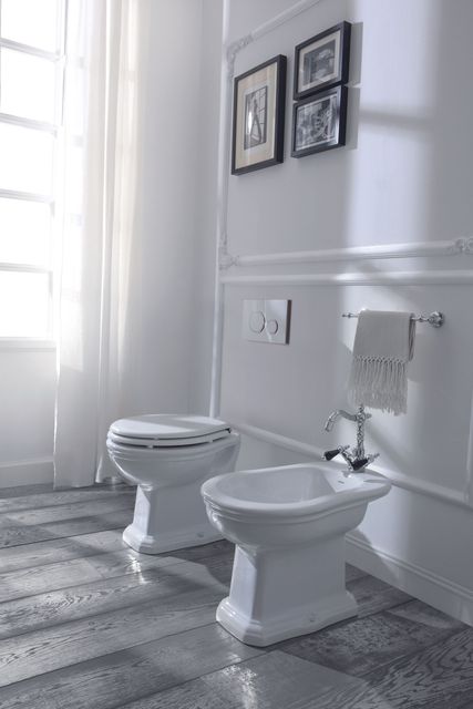 WC e bidet bianchi in un bagno con finestra e quadri incorniciati alla parete.