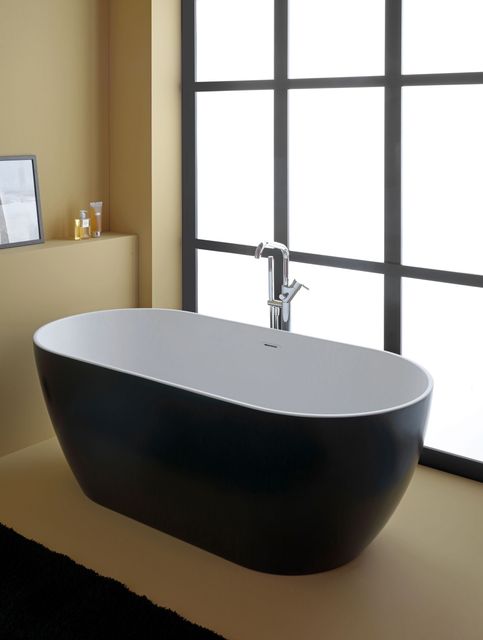 Vasca da bagno ovale bianca e nera in un bagno, accanto a una grande finestra.