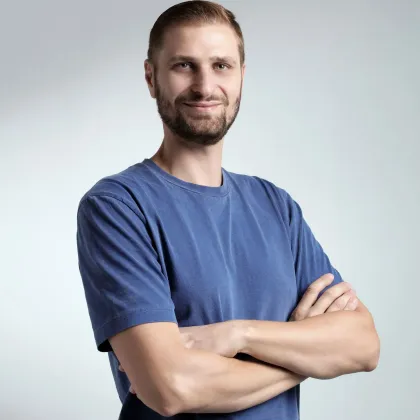 Uomo con la barba, braccia incrociate, maglietta blu, sorridente verso la telecamera.
