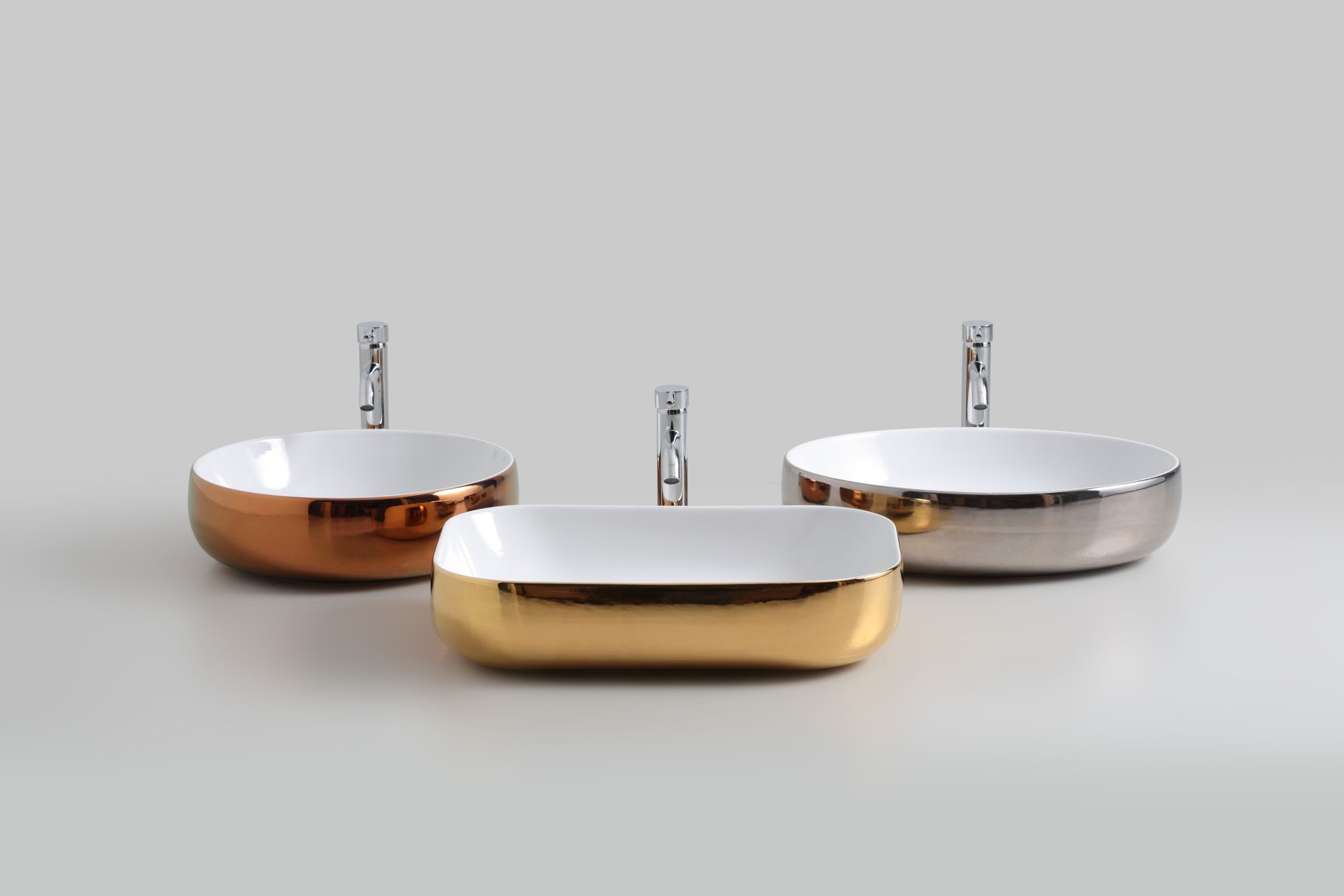 Tre lavandini da bagno in porcellana bianca con finiture metalliche e rubinetti su uno sfondo chiaro.
