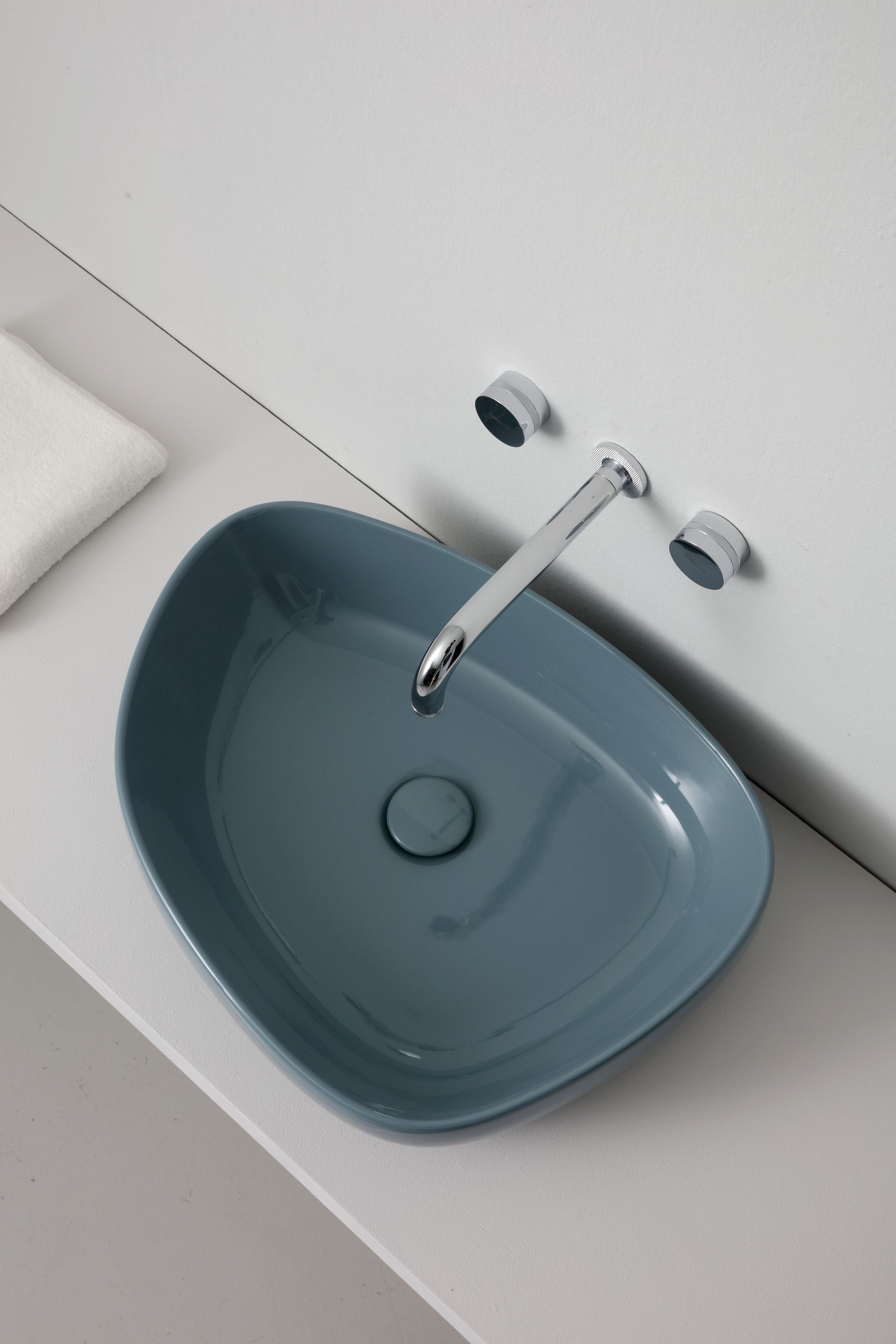 Lavandino ovale blu con rubinetto cromato su piano di lavoro bianco.