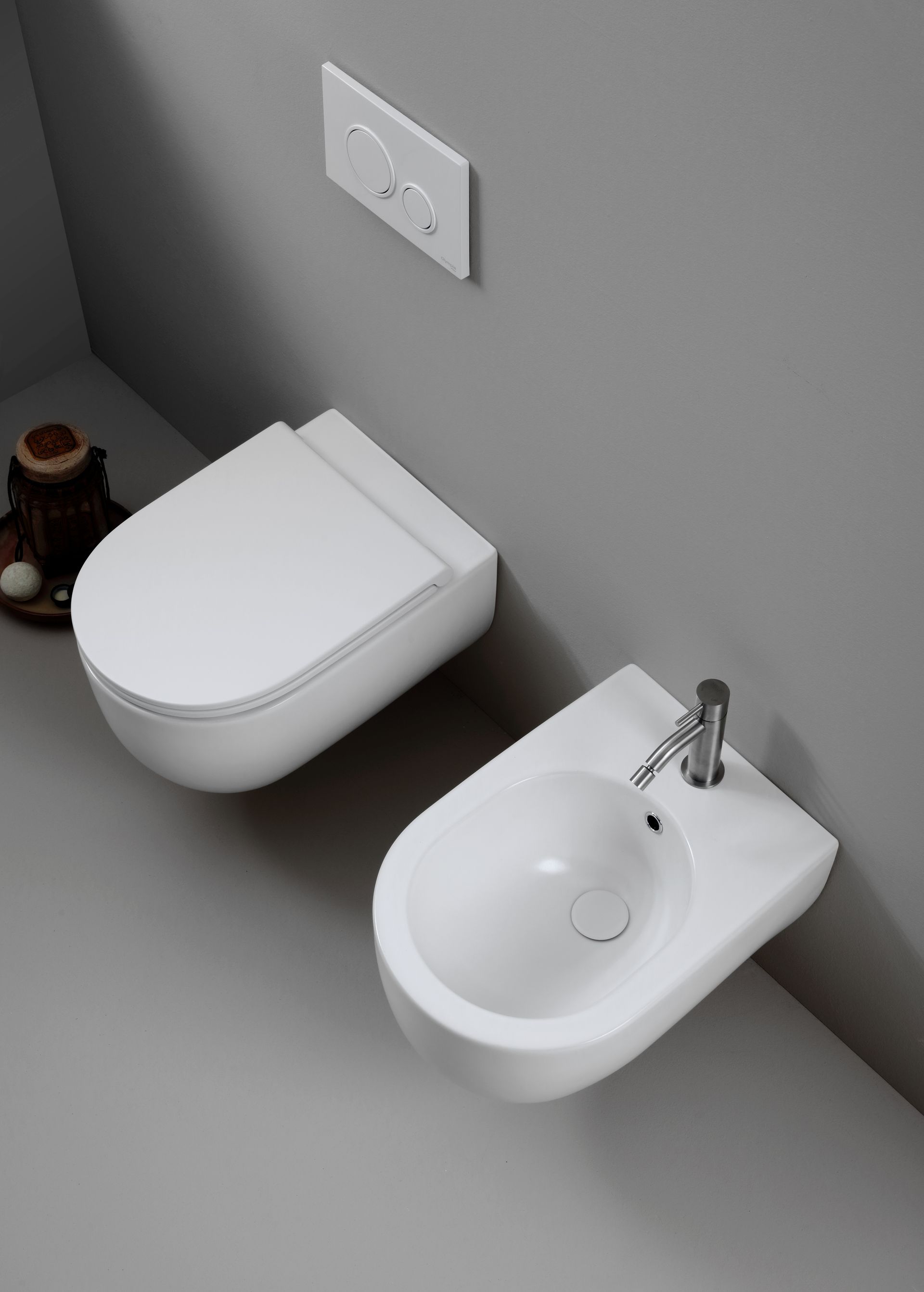WC e bidet bianchi contro una parete grigia in un bagno minimalista.