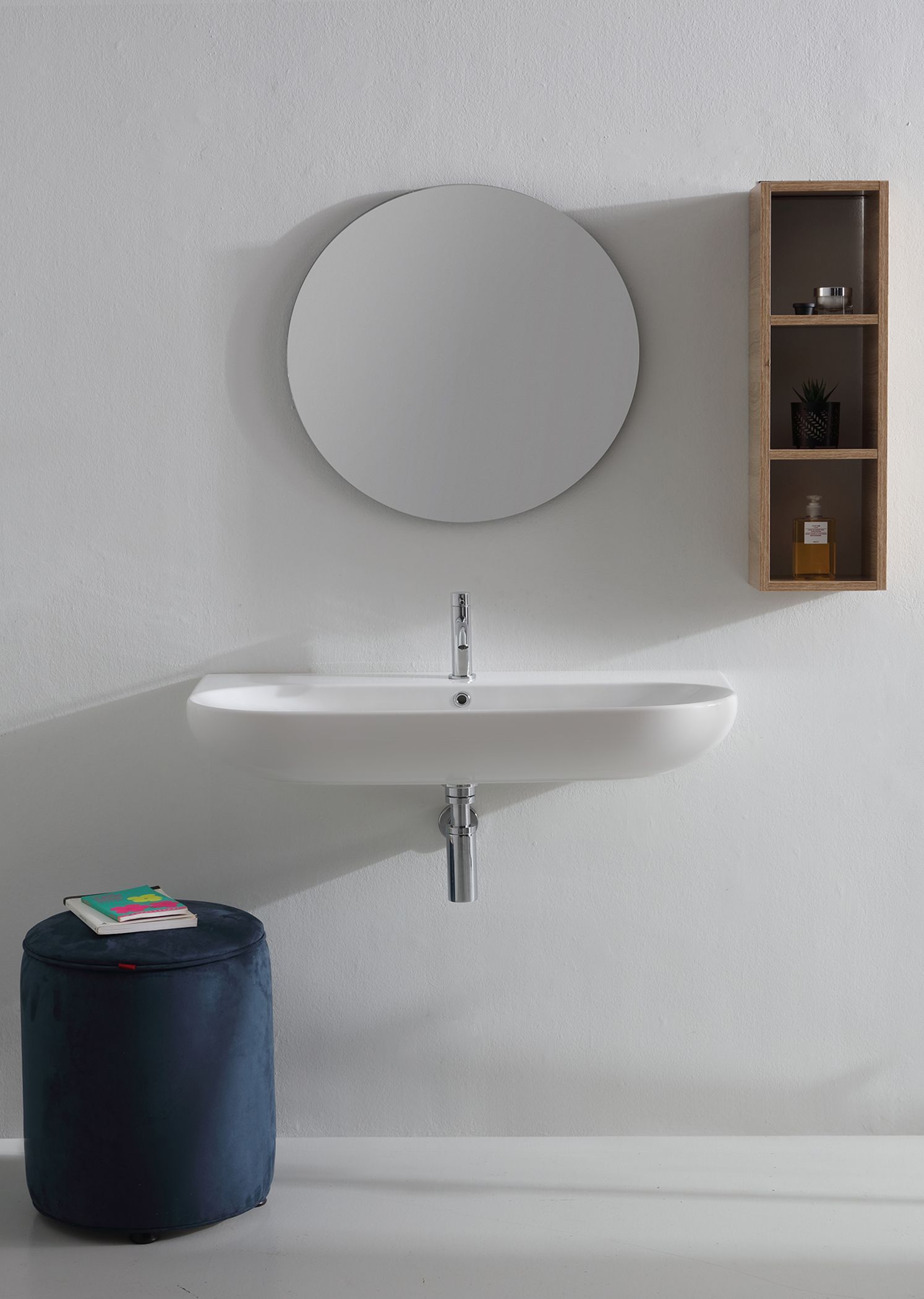 Bagno con parete bianca, specchio, lavandino, mensola in legno e pouf blu.