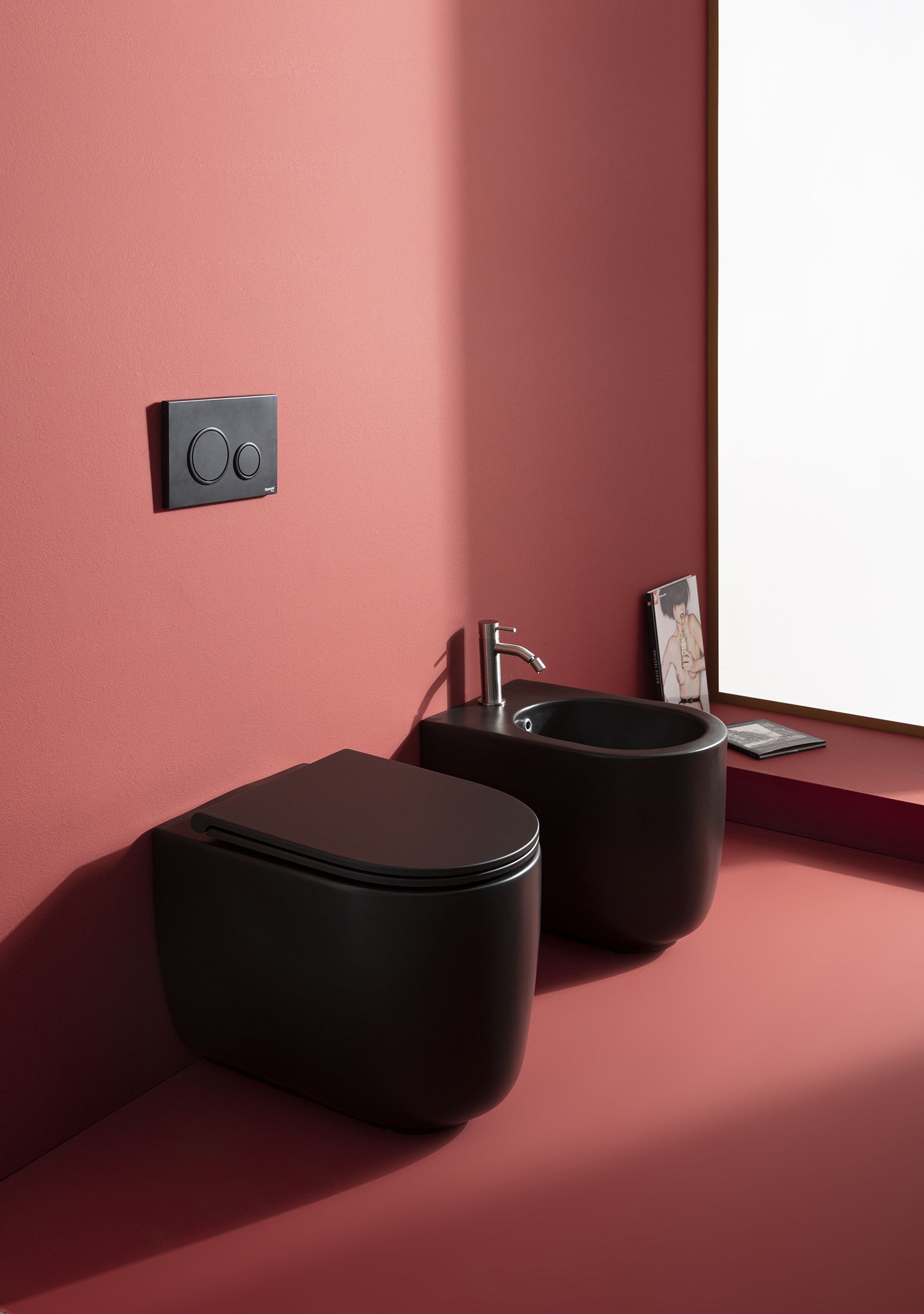 WC e bidet neri in un bagno con pareti rosse. Pulsanti di scarico a parete.