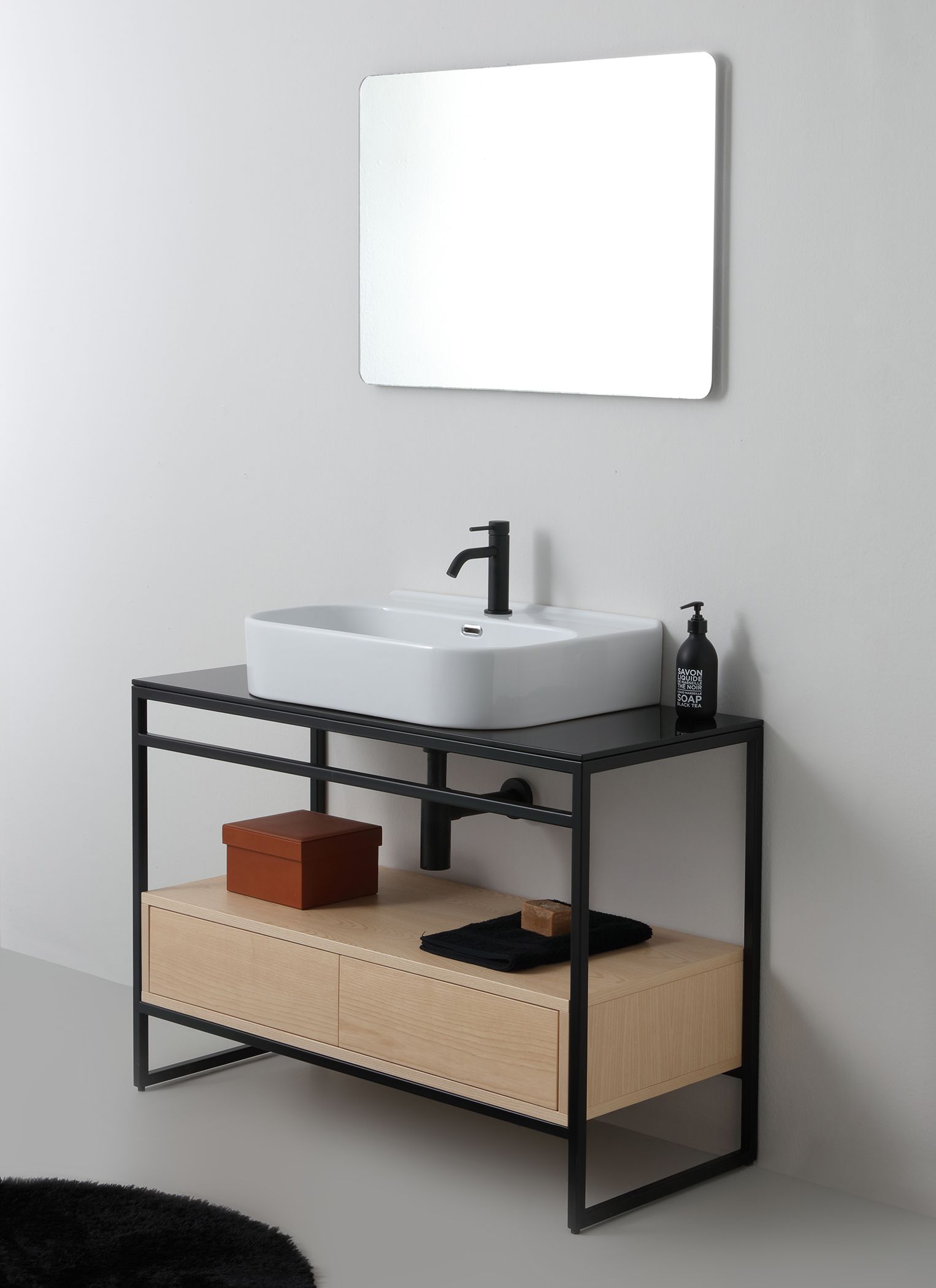 Mobile da bagno moderno con struttura in metallo nero, lavabo a appoggio e mobiletto in legno. Sopra è appeso uno specchio.