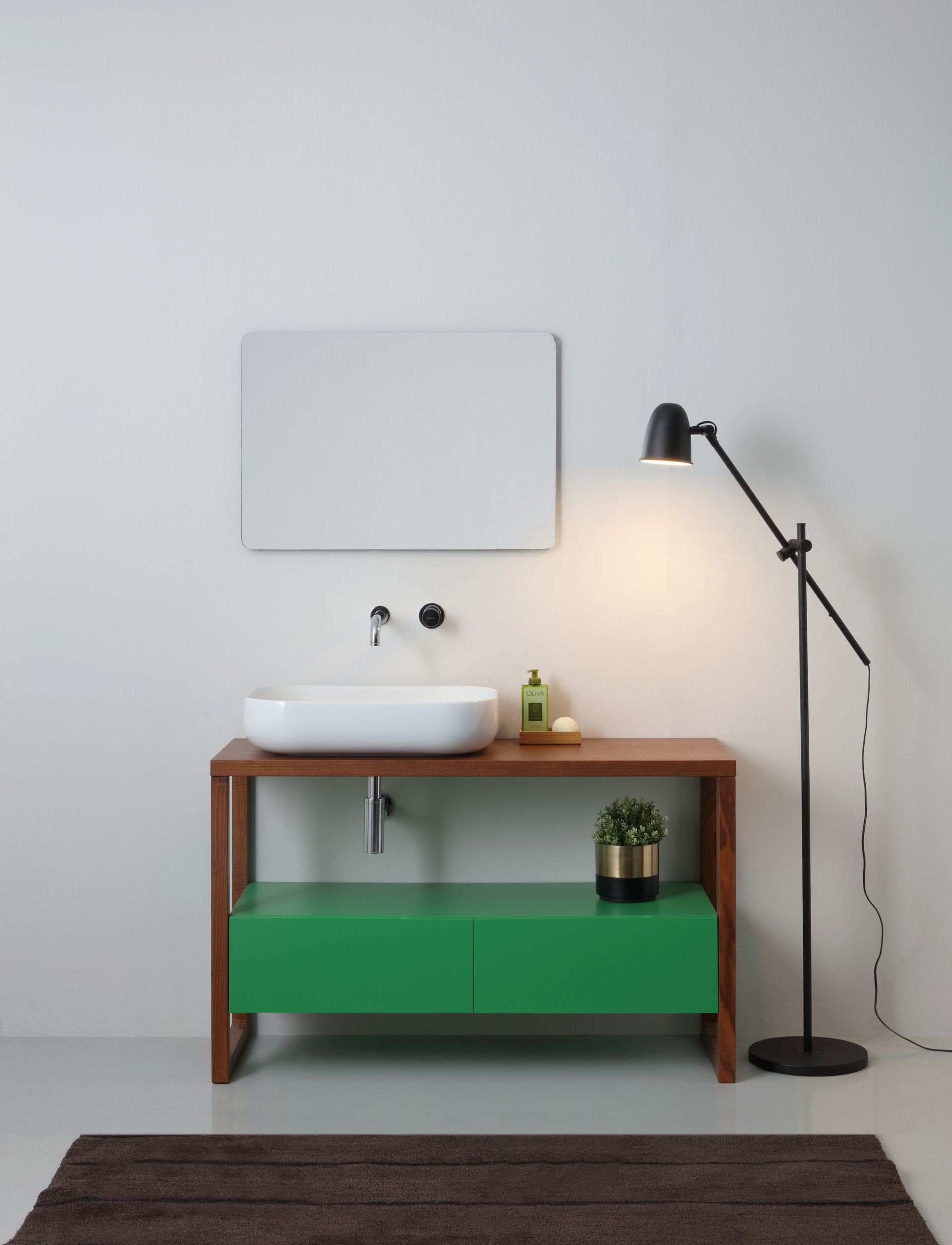 Mobiletto da bagno con mobiletto verde, piano di lavoro marrone, lavandino bianco, rubinetto nero, specchio e lampada.