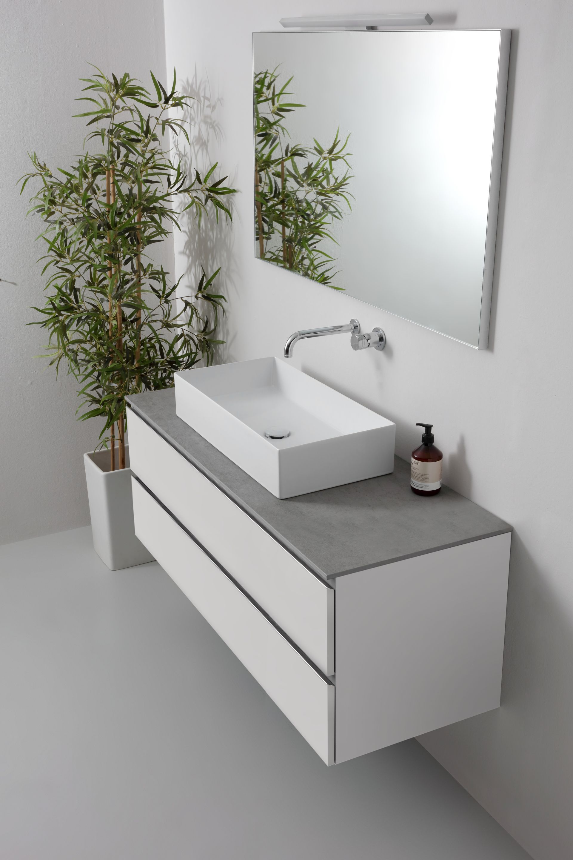Bagno moderno con mobile lavabo sospeso bianco, piano d'appoggio grigio, lavandino rettangolare, specchio e pianta di bambù.
