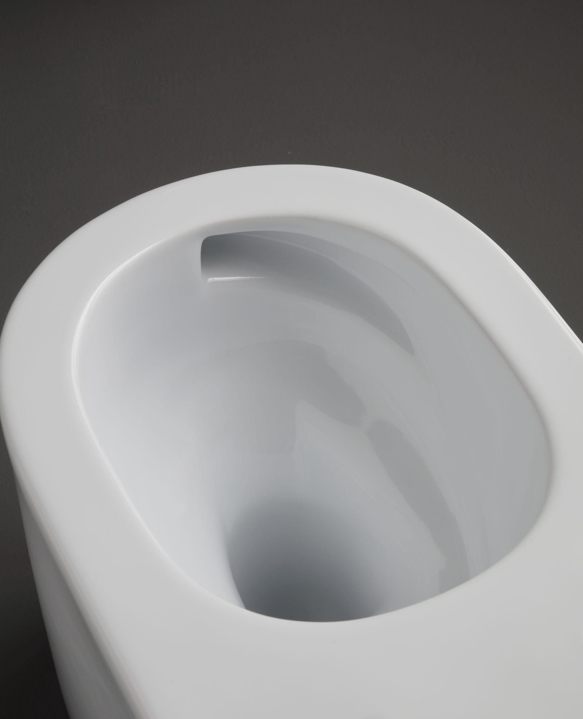 Tazza del water bianca, di forma ovale, vista dall'alto, su sfondo grigio.
