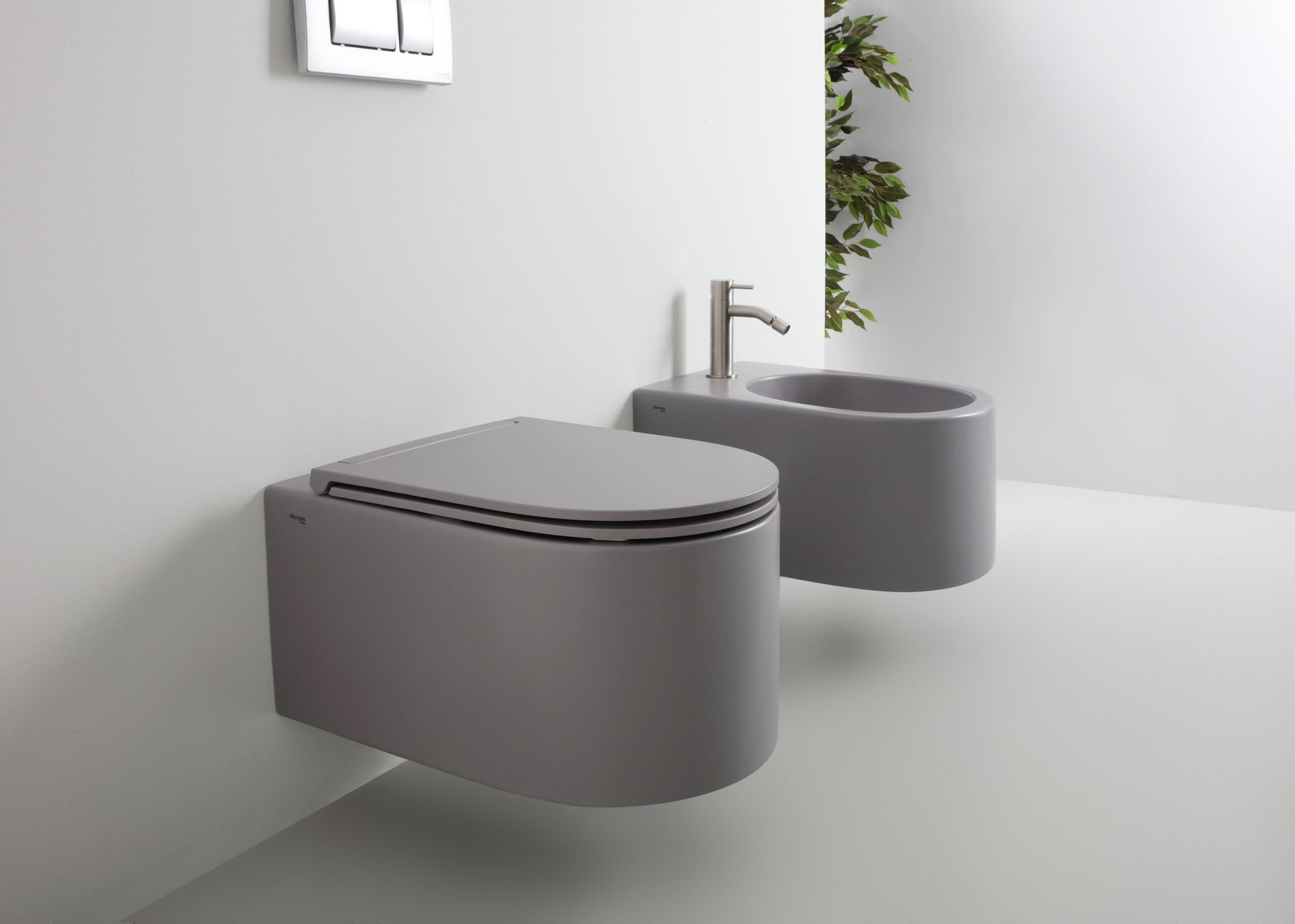 WC e bidet grigi sospesi in un bagno moderno e minimalista con rubinetto argentato e pareti bianche.