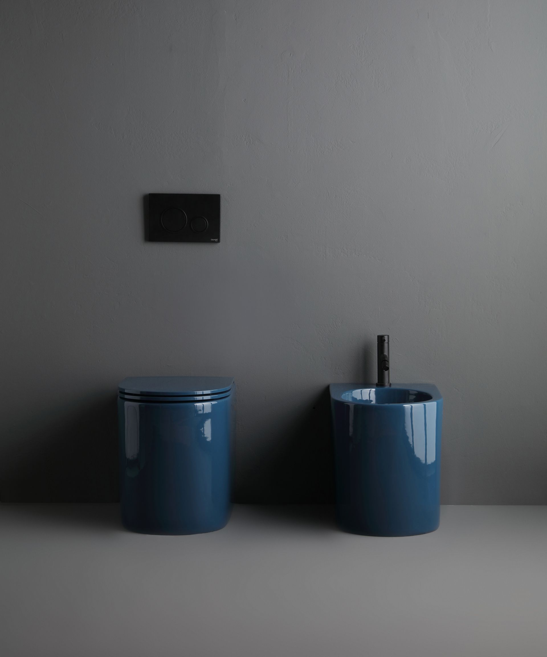 WC e bidet blu contro una parete grigia, con un pannello di controllo nero sopra.