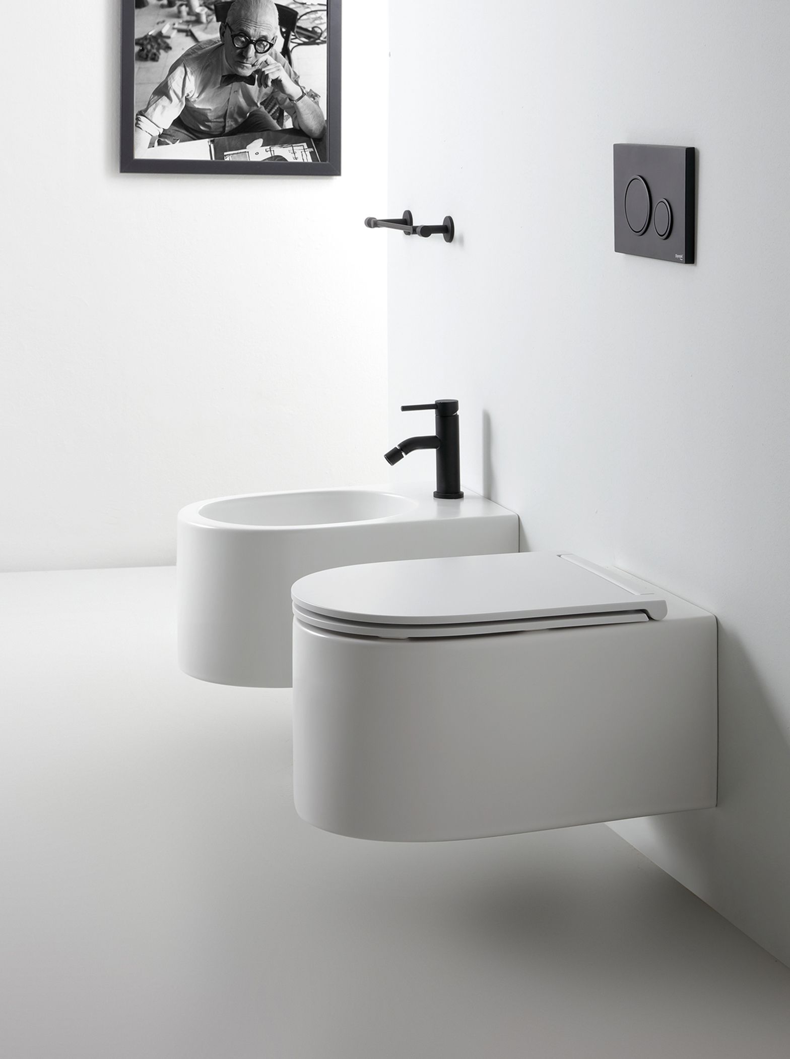 Bagno moderno, bianco, con WC e bidet sospesi, sanitari neri e quadri alle pareti.