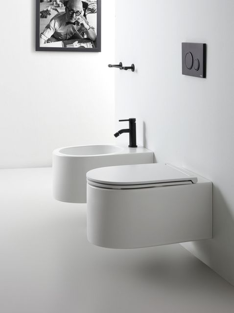 Moderno bagno bianco con WC e bidet sospesi, sanitari neri e un'opera d'arte.