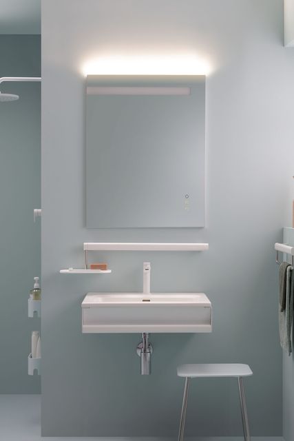 Bagno moderno con lavandino bianco, specchio con luce sopraelevata e un piccolo sgabello. Pareti azzurre.