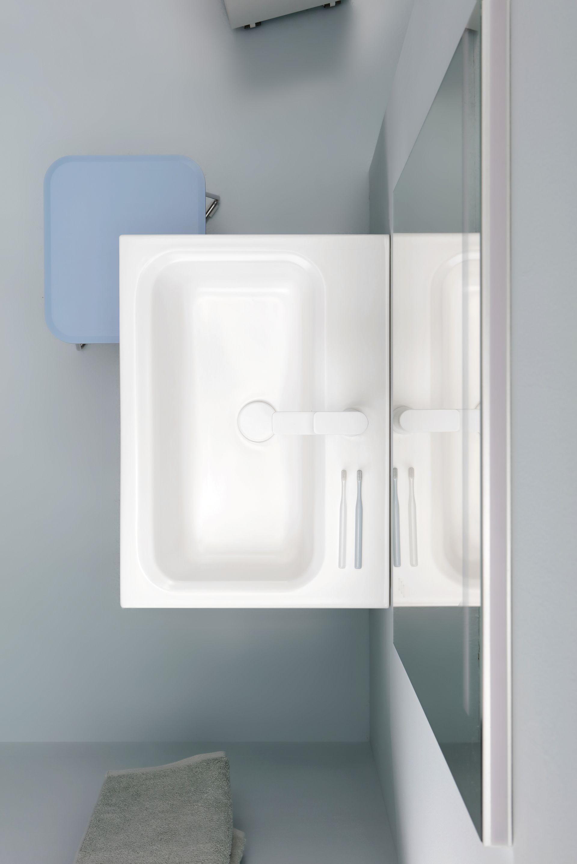 Lavandino bianco del bagno con specchio, parete azzurra, scatola blu sul muro e un asciugamano sul pavimento.