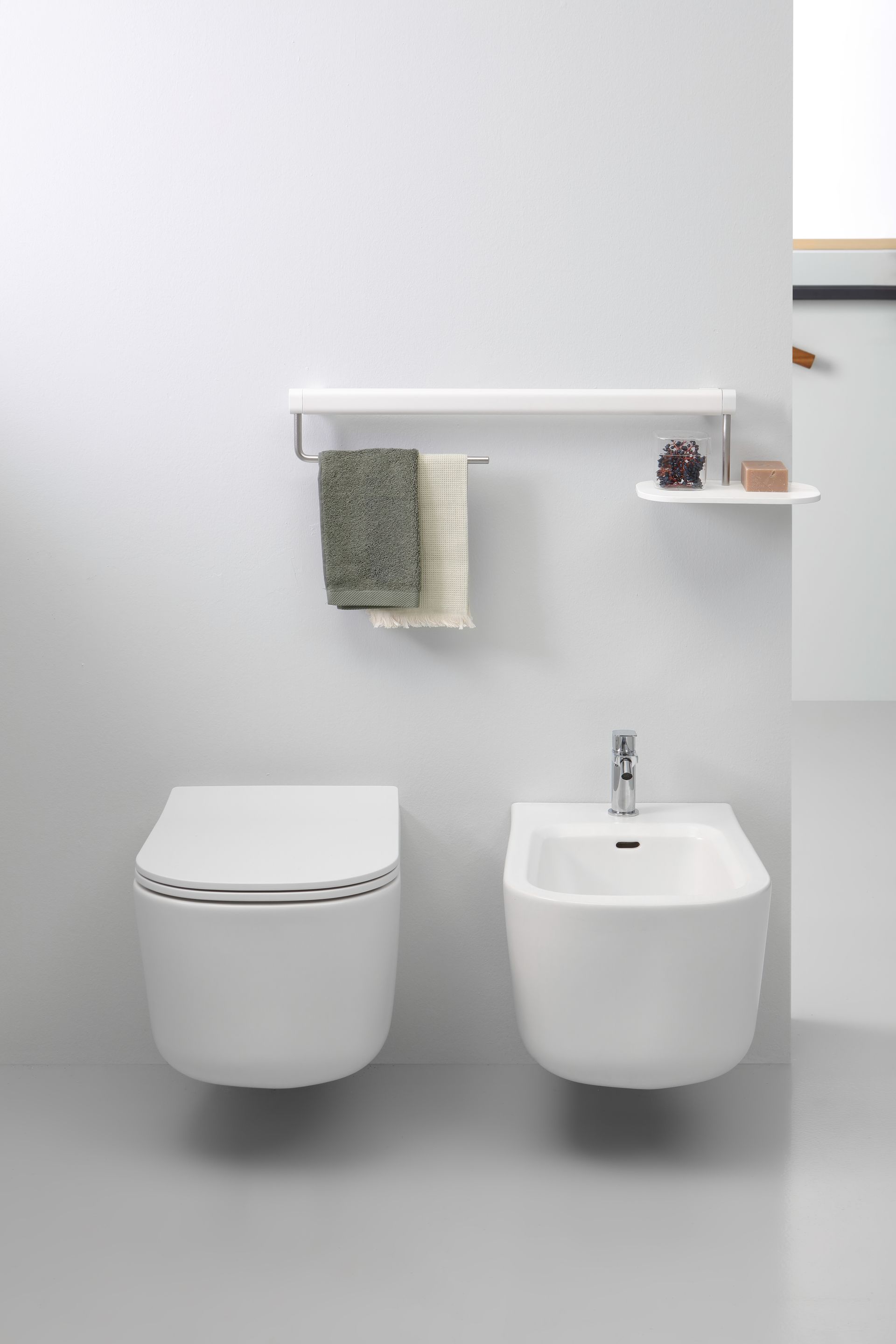 Moderno WC e bidet bianchi sospesi in un ambiente bagno minimalista, con portasciugamani e mensola.