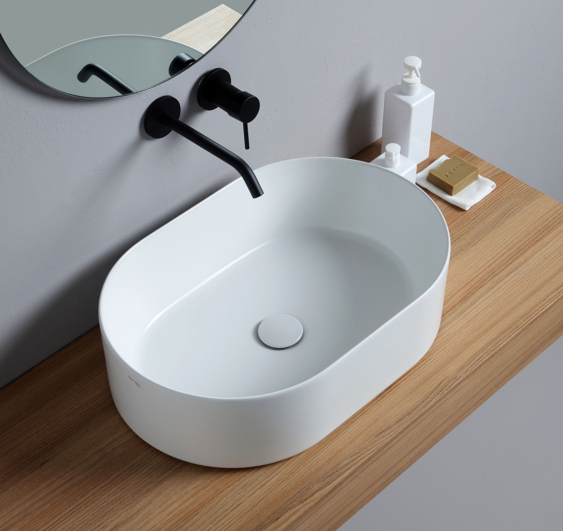 Lavandino ovale in ceramica bianca su piano in legno con rubinetto nero.