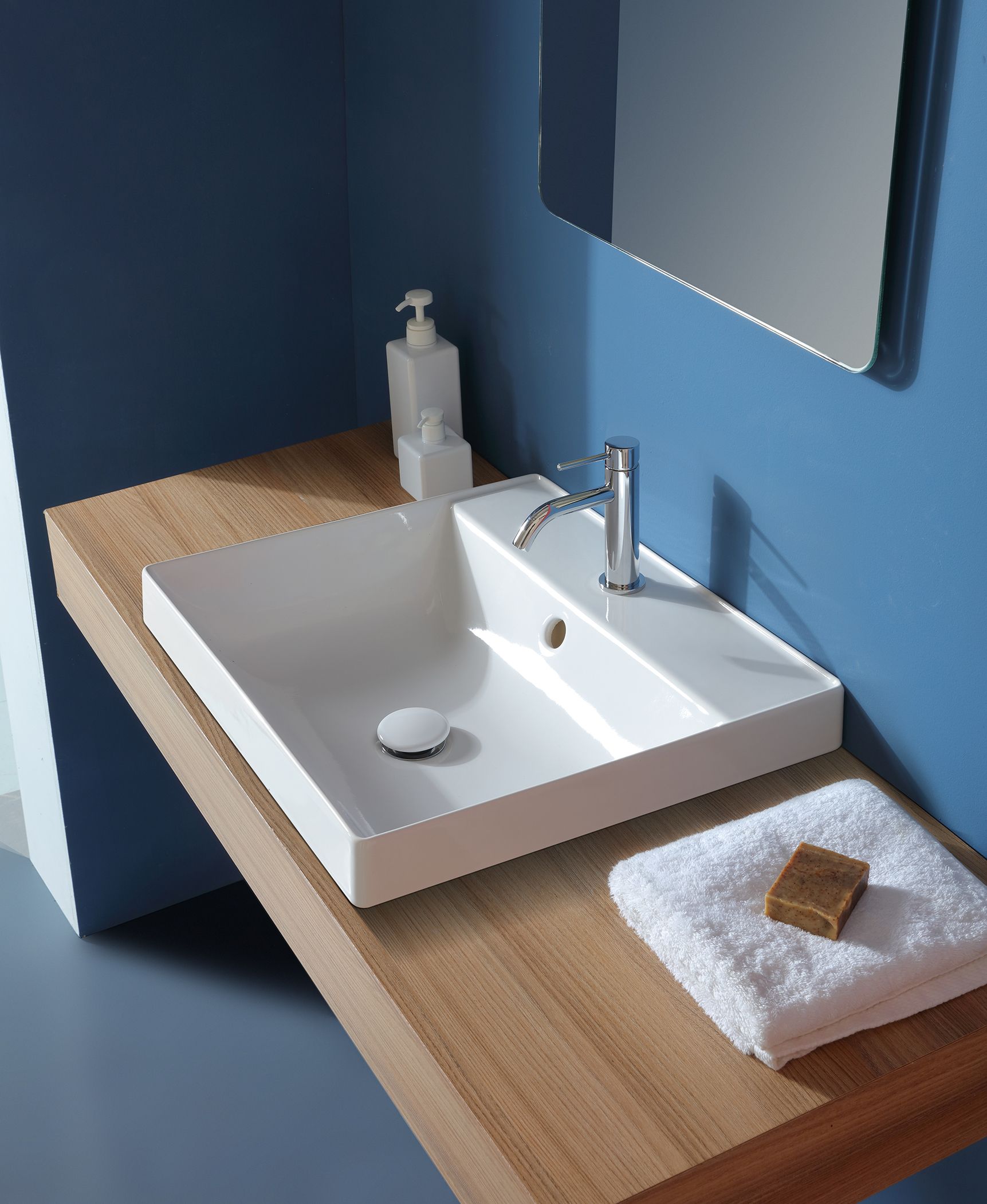 Lavandino rettangolare bianco con rubinetto su ripiano in legno in un bagno blu.