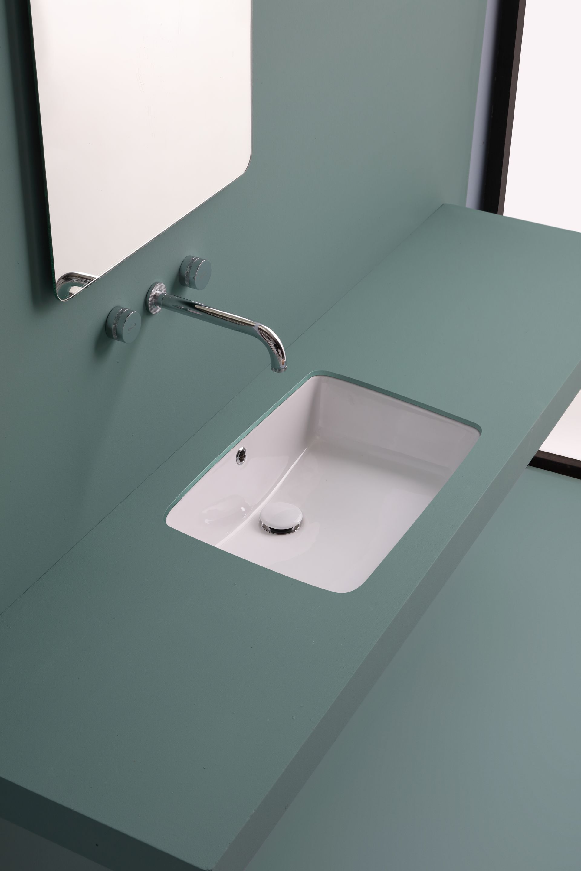 Lavandino bianco su ripiano verde acqua, rubinetto cromato, specchio.