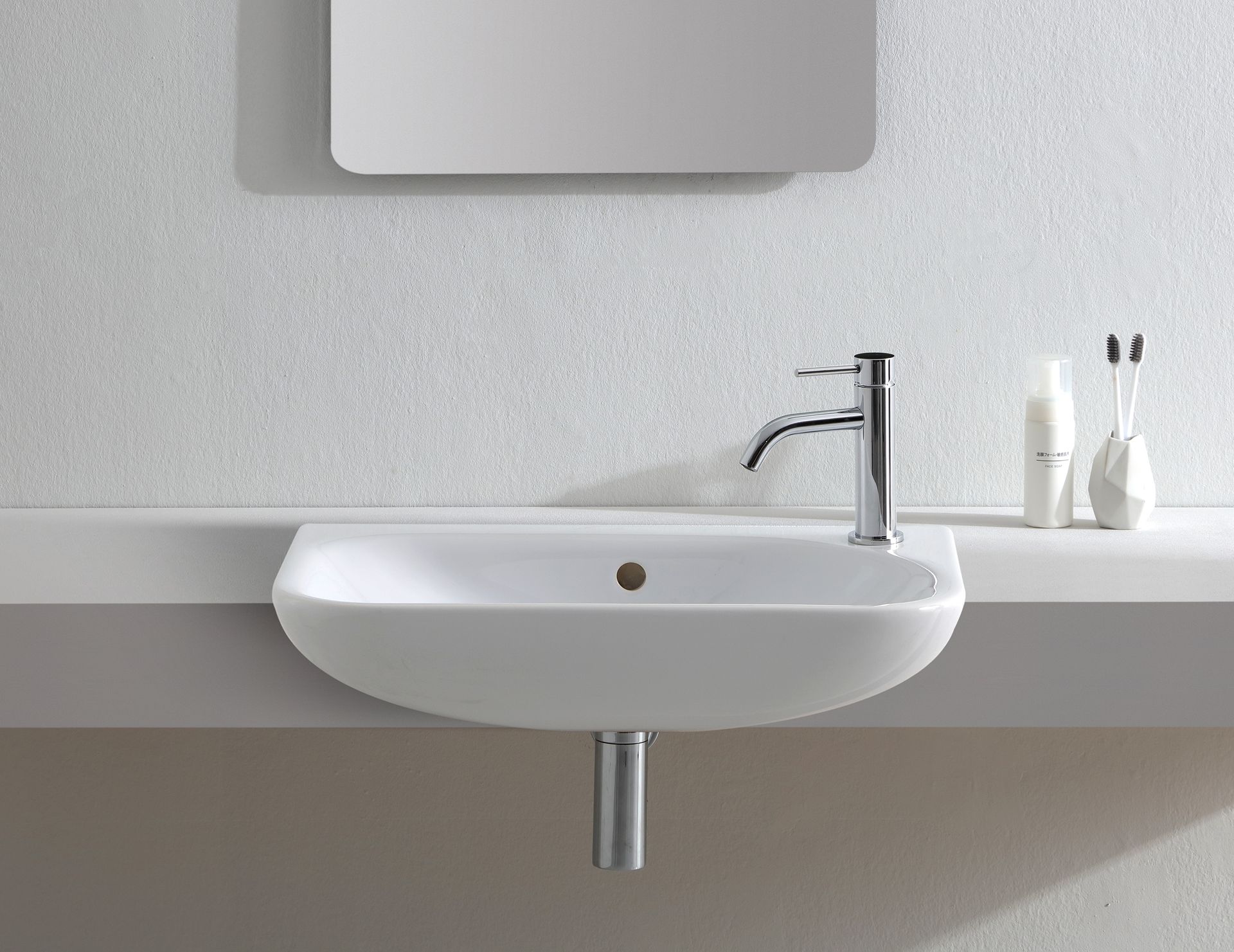 Lavandino in ceramica bianca con rubinetto cromato, sotto uno specchio, su un piano di lavoro bianco.
