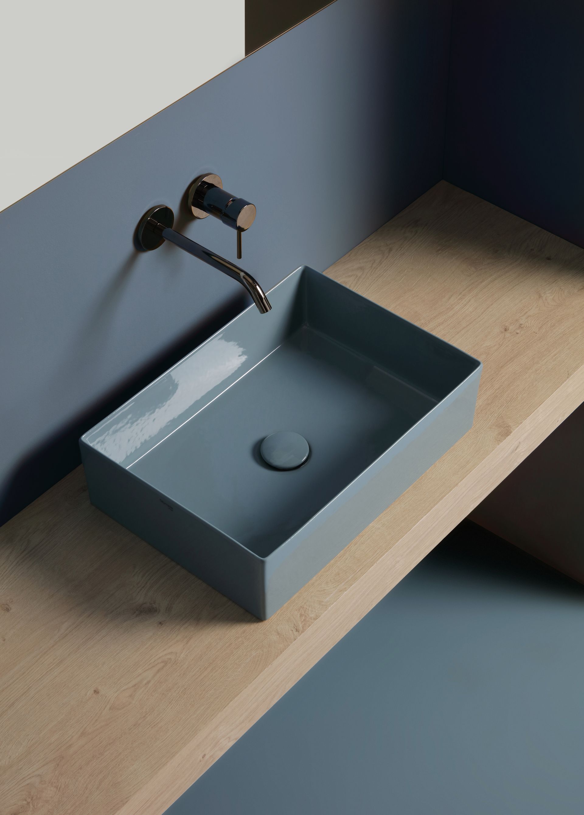 Lavandino rettangolare blu su mensola color cuoio con rubinetto a parete. Sfondo blu e marrone.