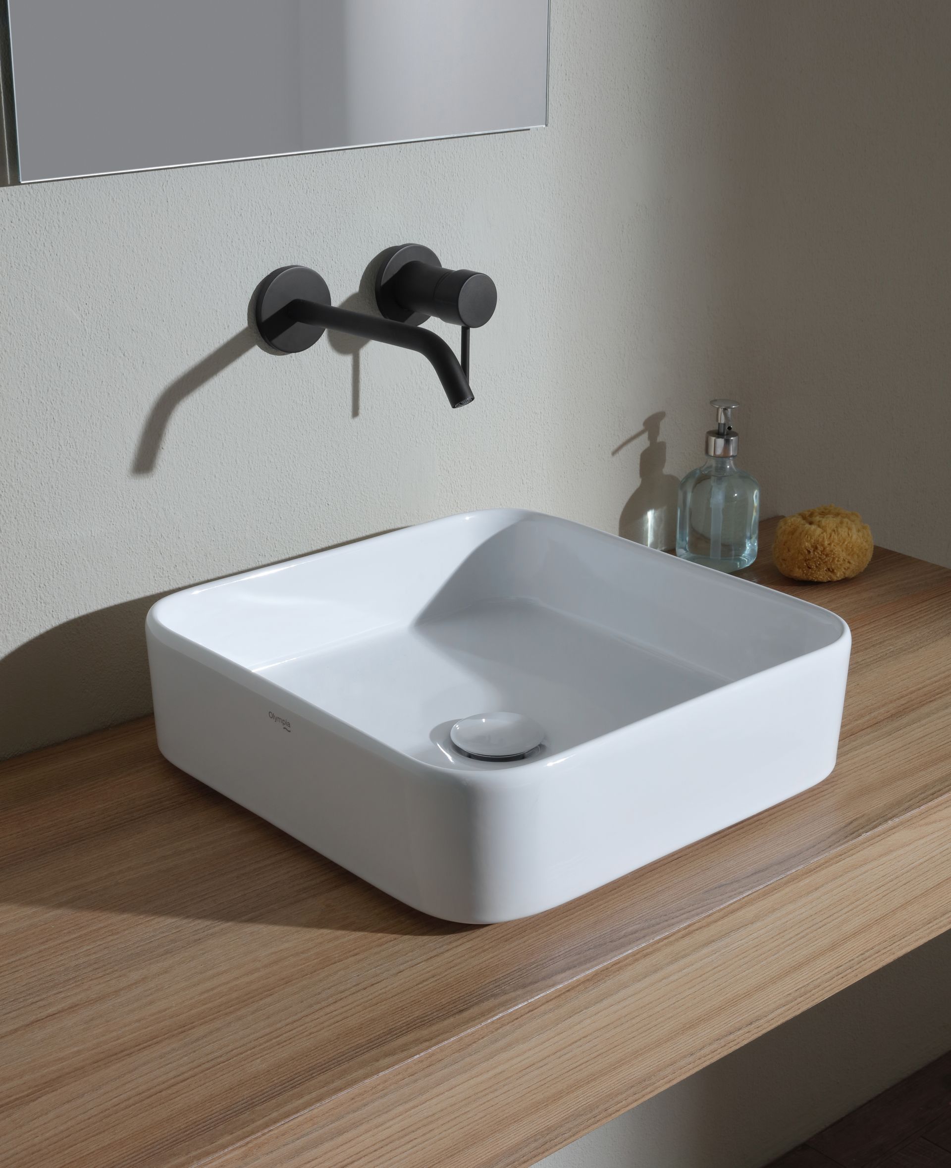 Lavandino bianco quadrato su un bancone in legno con rubinetto nero opaco e dispenser di sapone liquido.