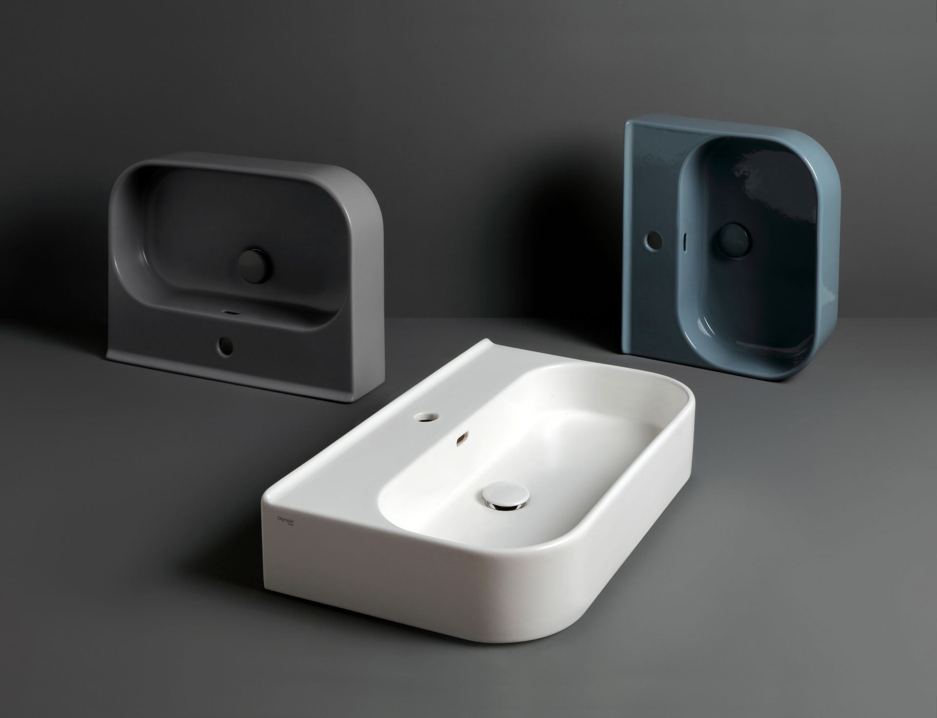 Tre moderni lavandini da bagno in grigio, blu e bianco, su uno sfondo grigio.