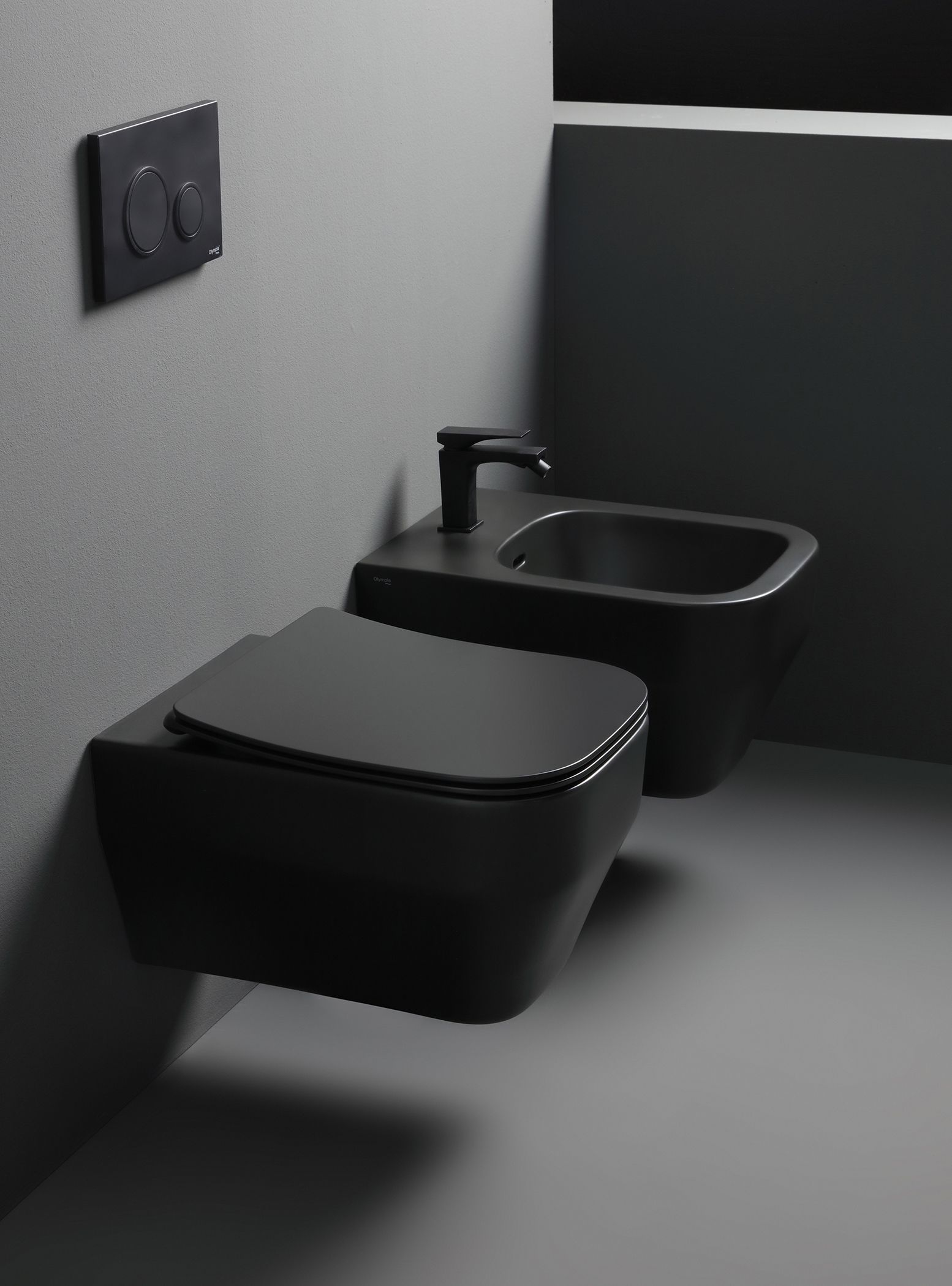 WC e bidet neri sospesi in un bagno grigio, con una placca di scarico sopra.