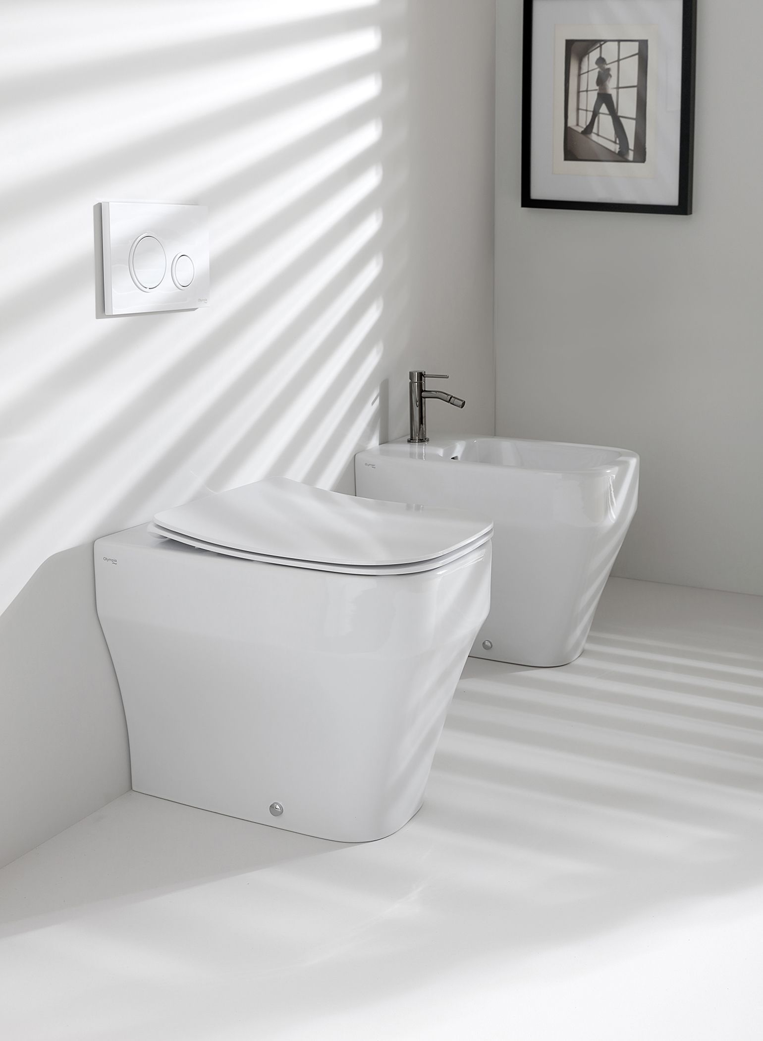 WC e bidet bianchi in un bagno luminoso, con ombra prodotta dalle tende e opere d'arte sulla parete.