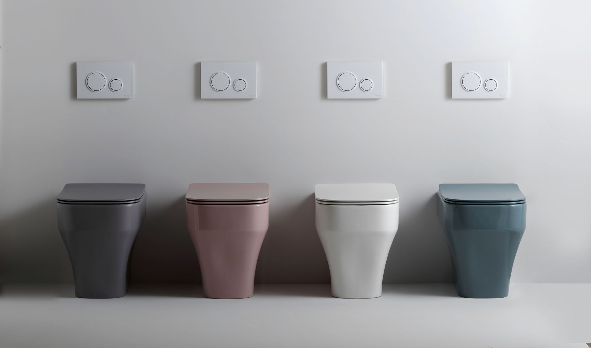 Quattro moderni water con coperchi colorati e pulsanti di scarico nella parte superiore.