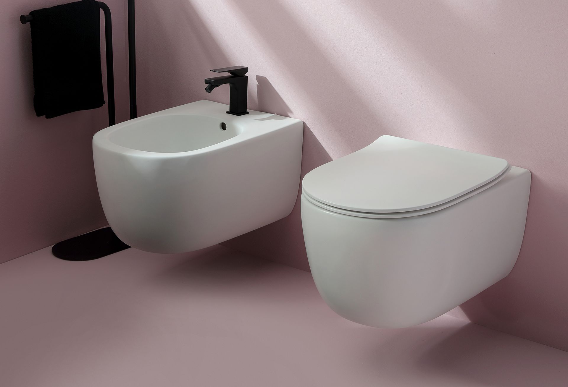 Bidet e WC bianchi sospesi in un bagno con pareti rosa e sanitari neri.