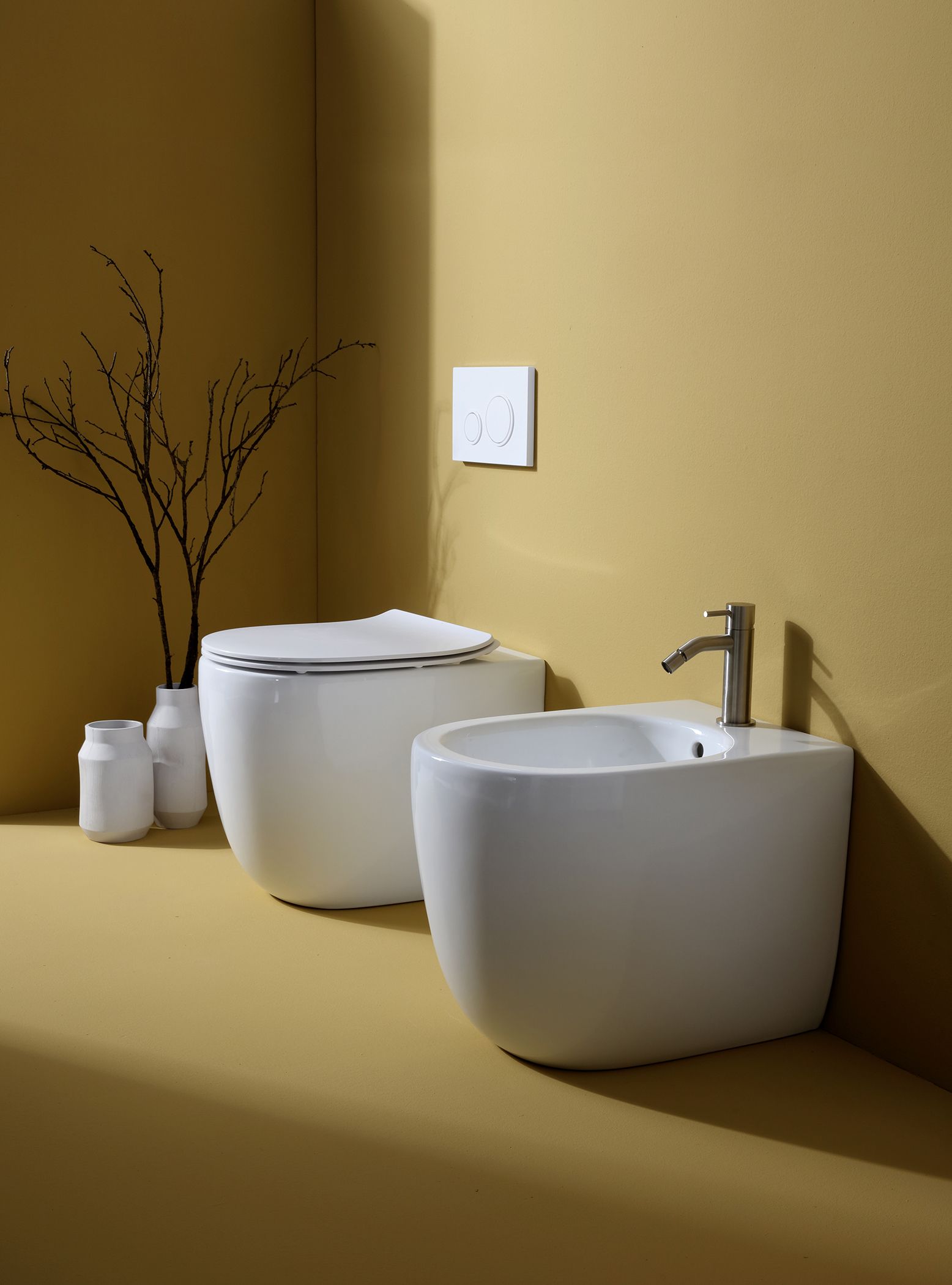WC e bidet bianchi in un bagno con pareti gialle, vasi decorativi e rubinetto.