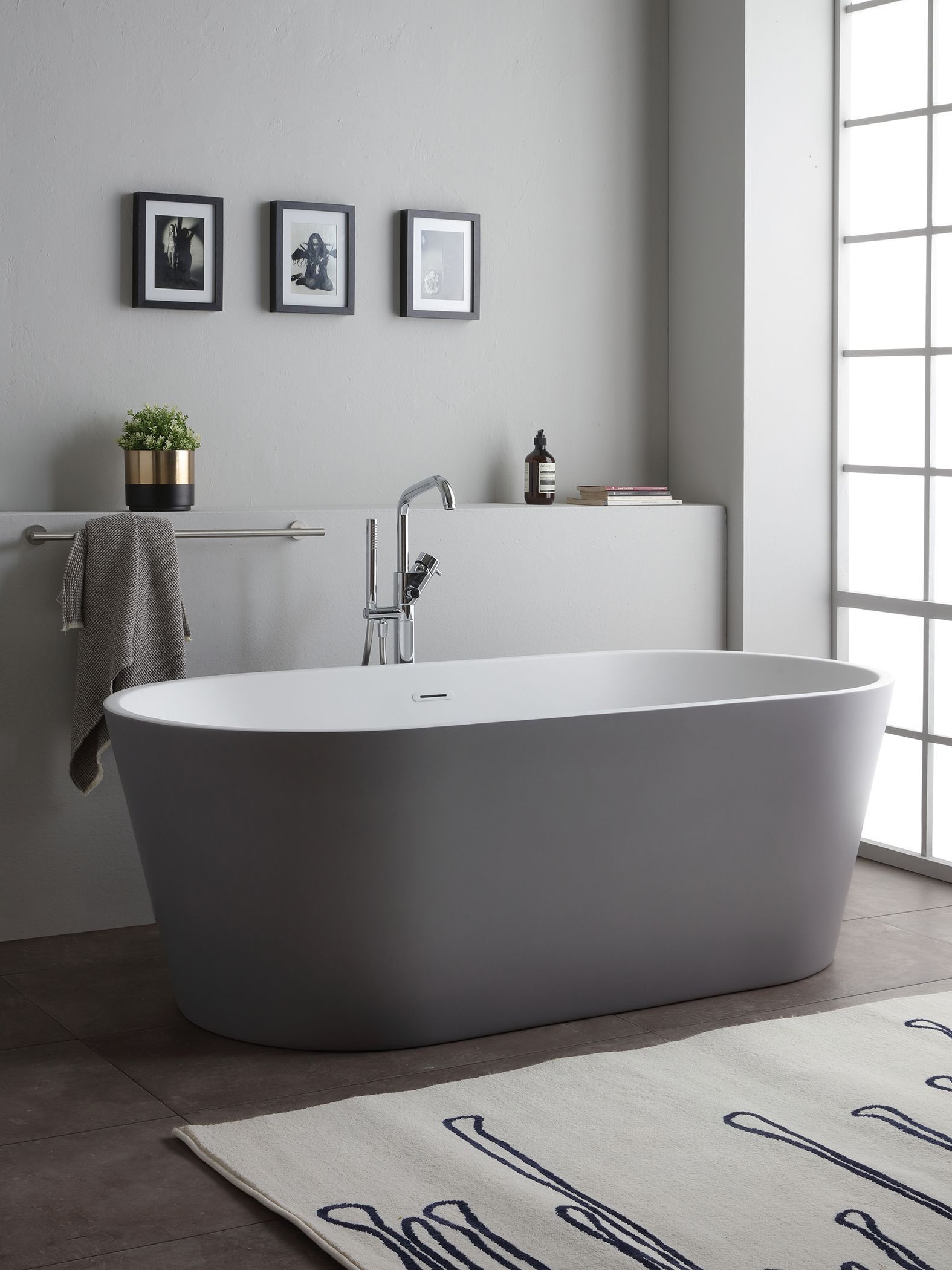 Bagno moderno con vasca ovale grigia, rubinetto argentato e oggetti decorativi.