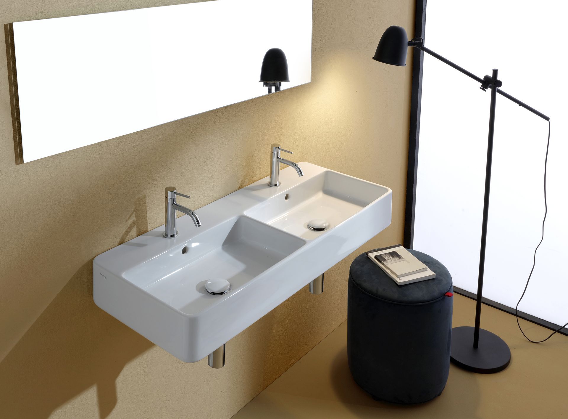 Moderno lavandino doppio bianco con due rubinetti, specchio a parete e lampada nera in un bagno.