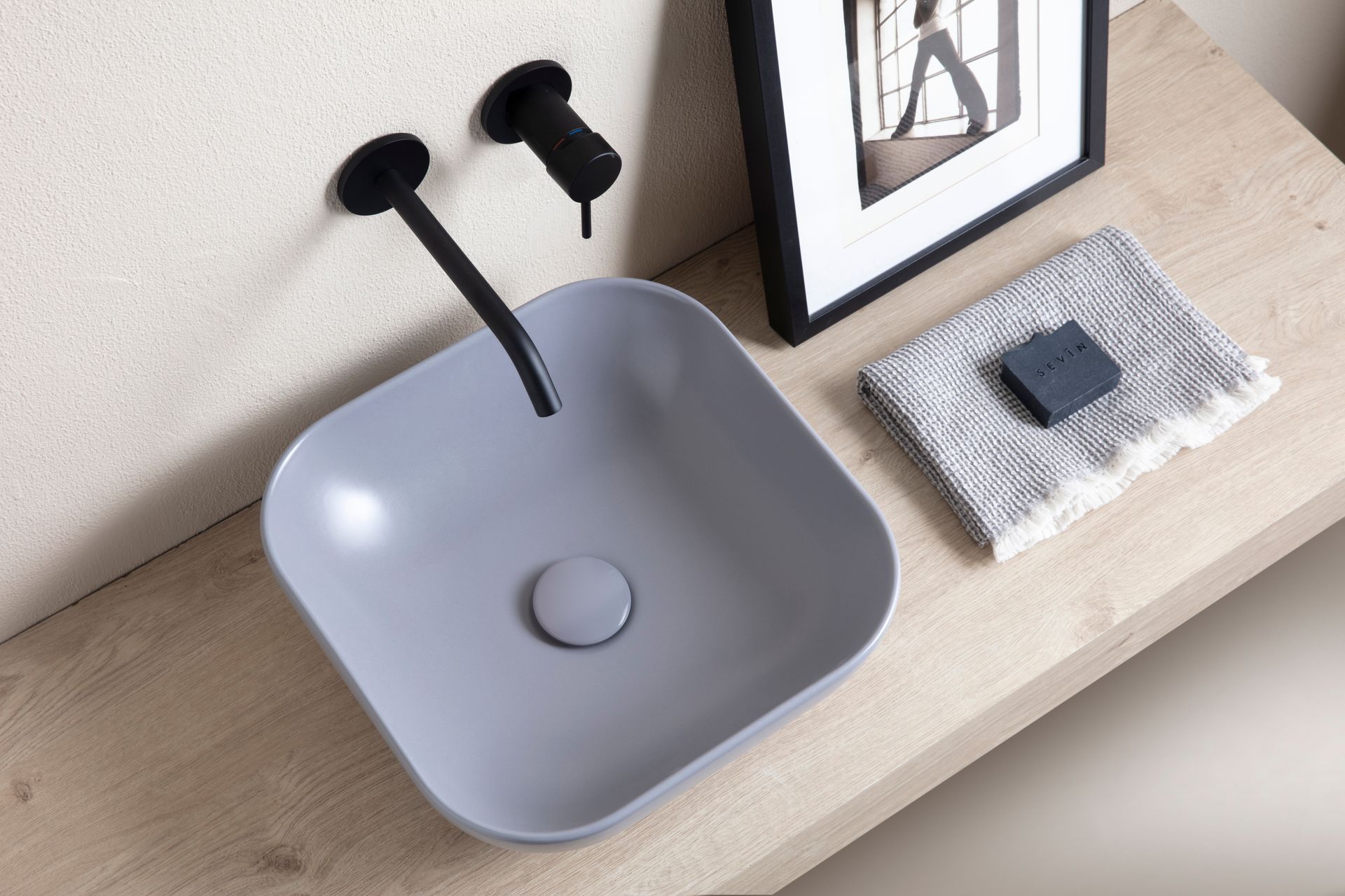Lavandino quadrato grigio con rubinetto nero, sapone e asciugamano su una mensola in legno.