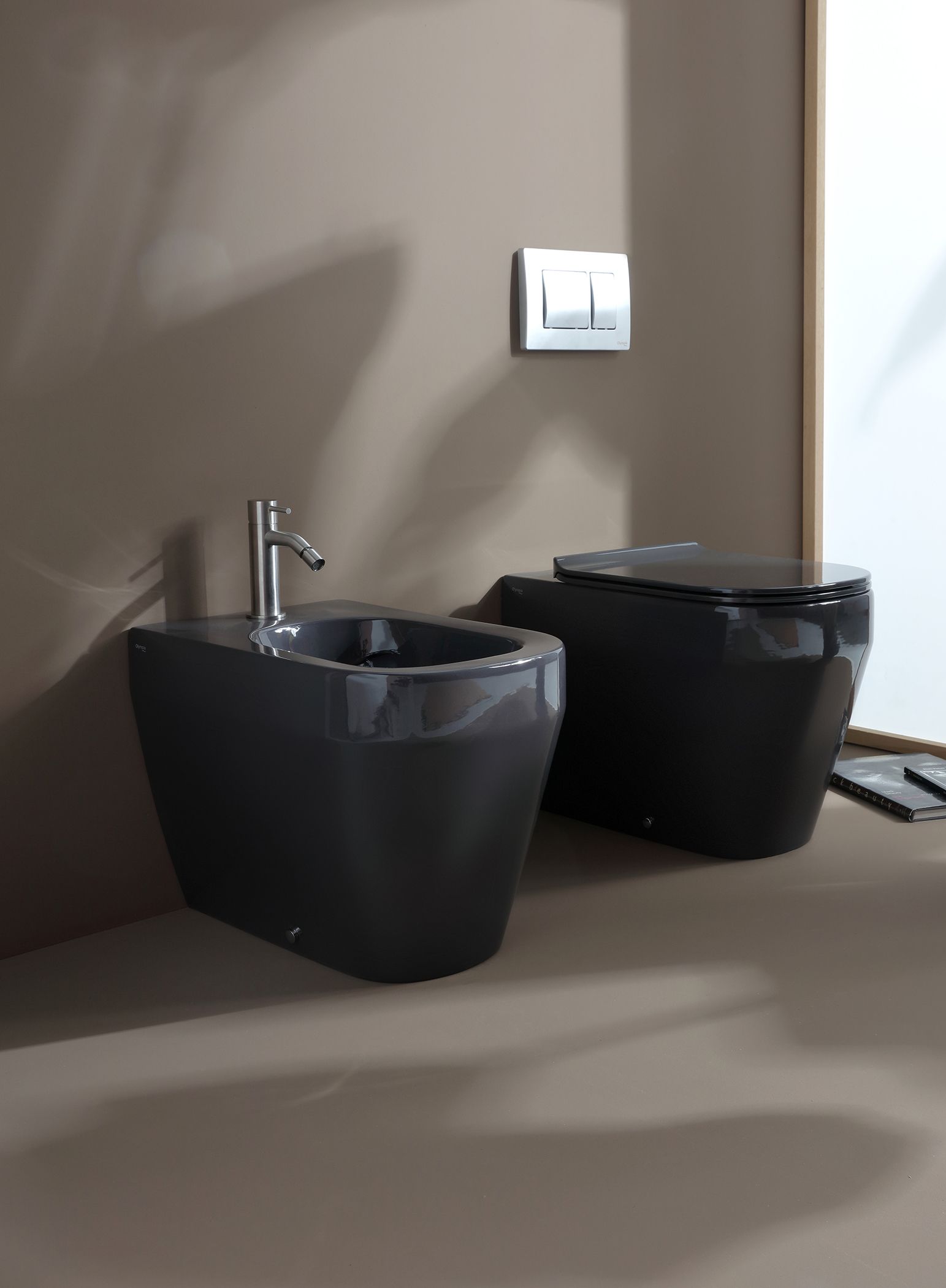 Due sanitari da bagno grigio scuro montati a parete: un bidet con rubinetto e un WC.