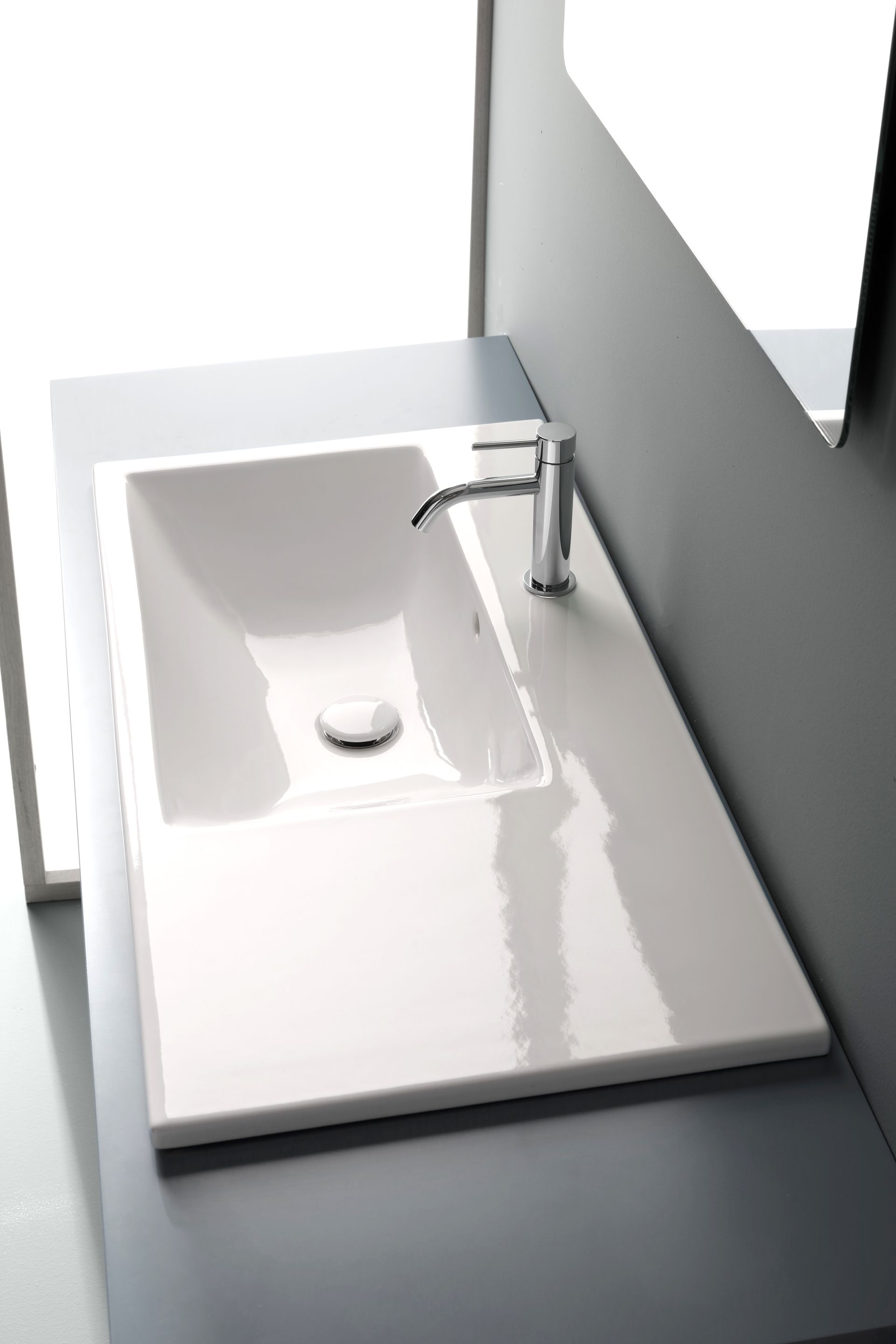 Lavandino rettangolare bianco con rubinetto cromato su piano di lavoro grigio.