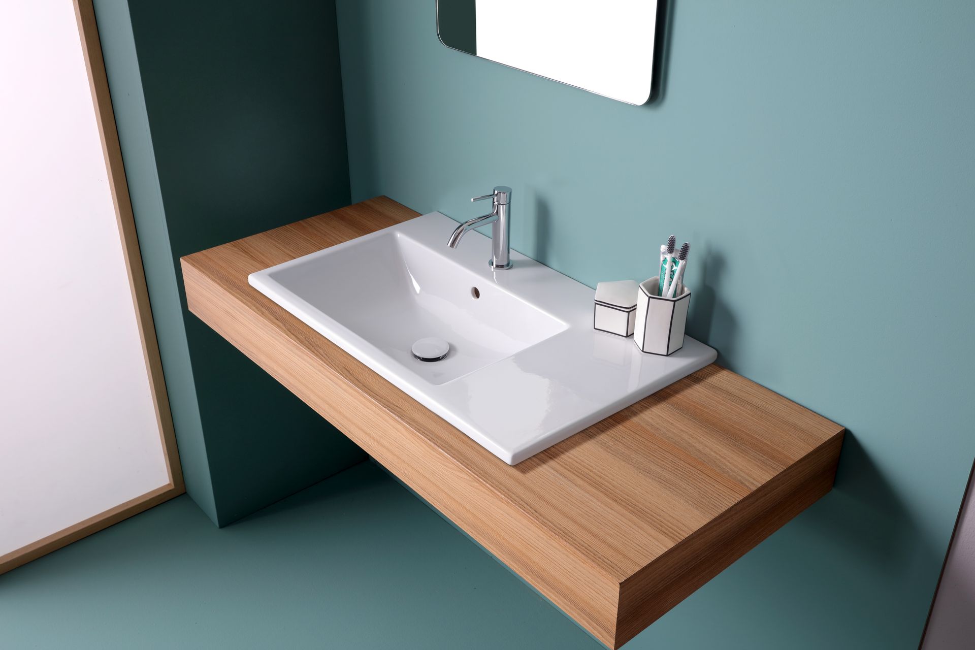 Lavandino bianco su bancone in legno con rubinetto cromato, specchio e articoli da toeletta in un bagno color verde acqua.