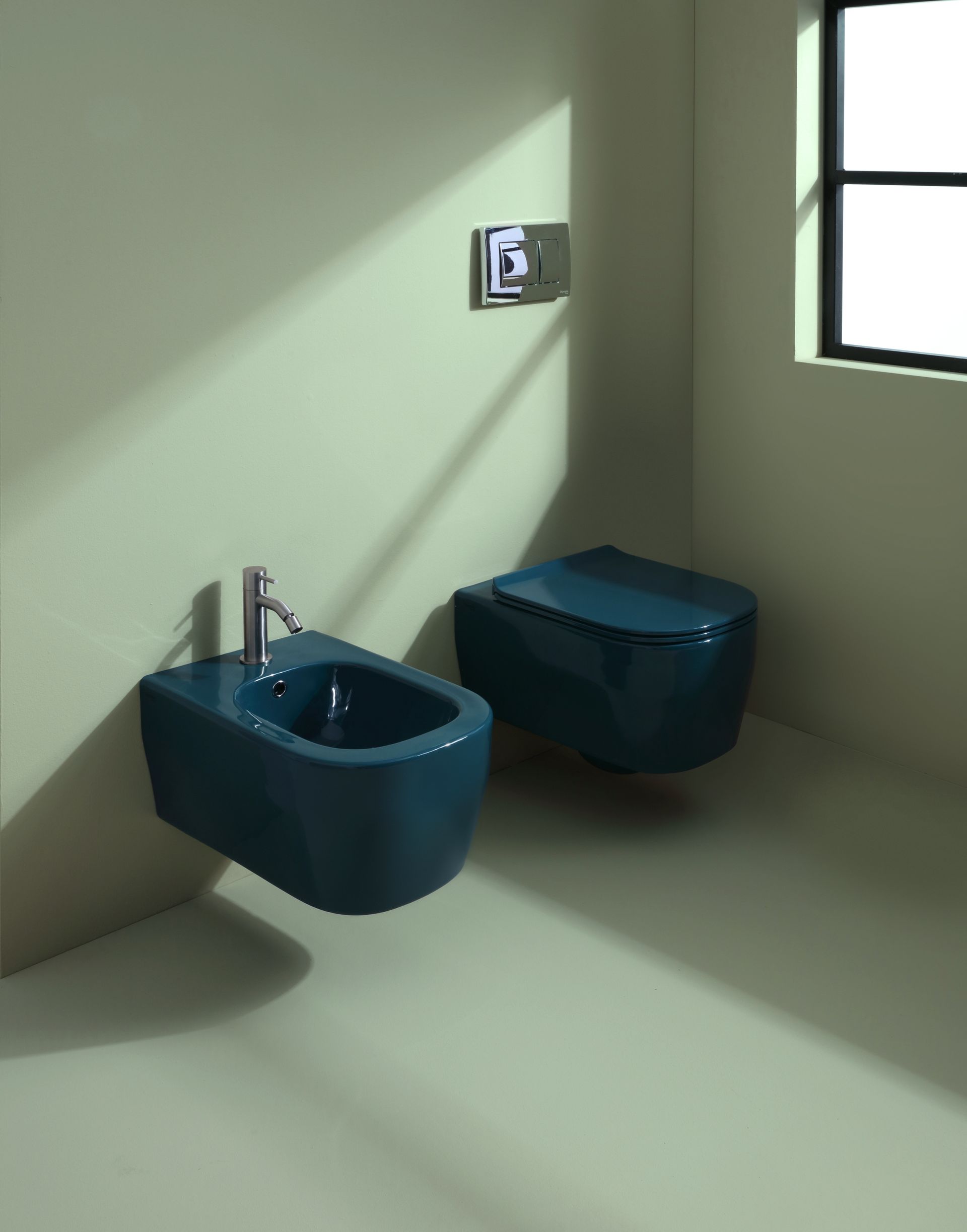 Sanitari blu per WC e bidet in un bagno angolare, con finestra e pannello di controllo sulla parete.