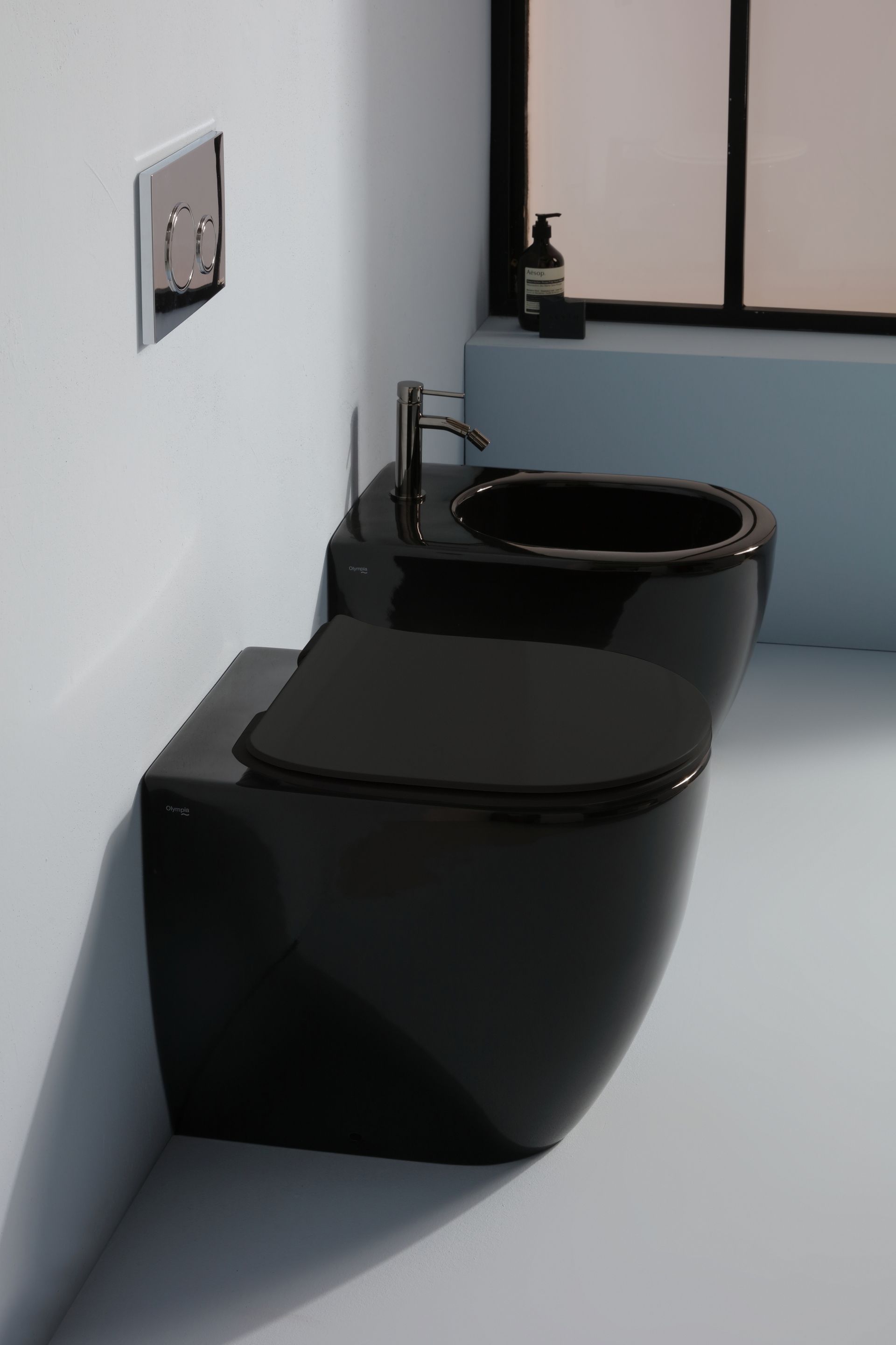 Combinazione di WC e bidet neri in un bagno moderno con finestra e comando di scarico a parete.