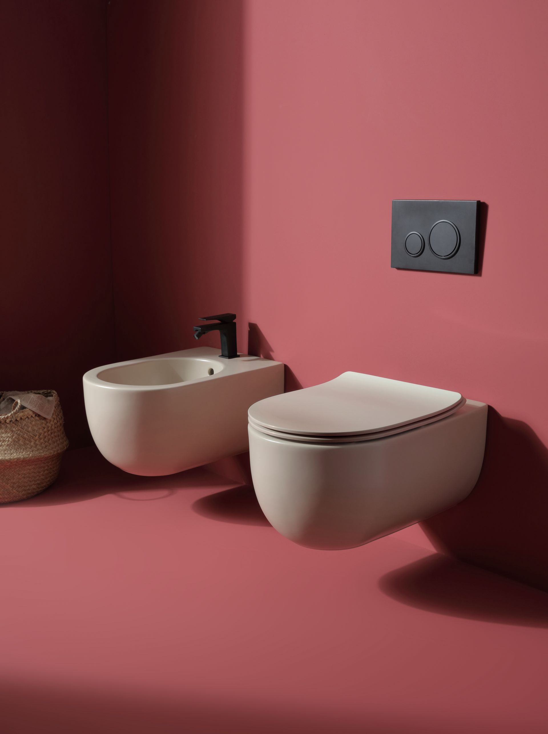 Bagno moderno con WC e bidet sospesi, color crema, su una parete rosa scuro. Ferramenta nera.