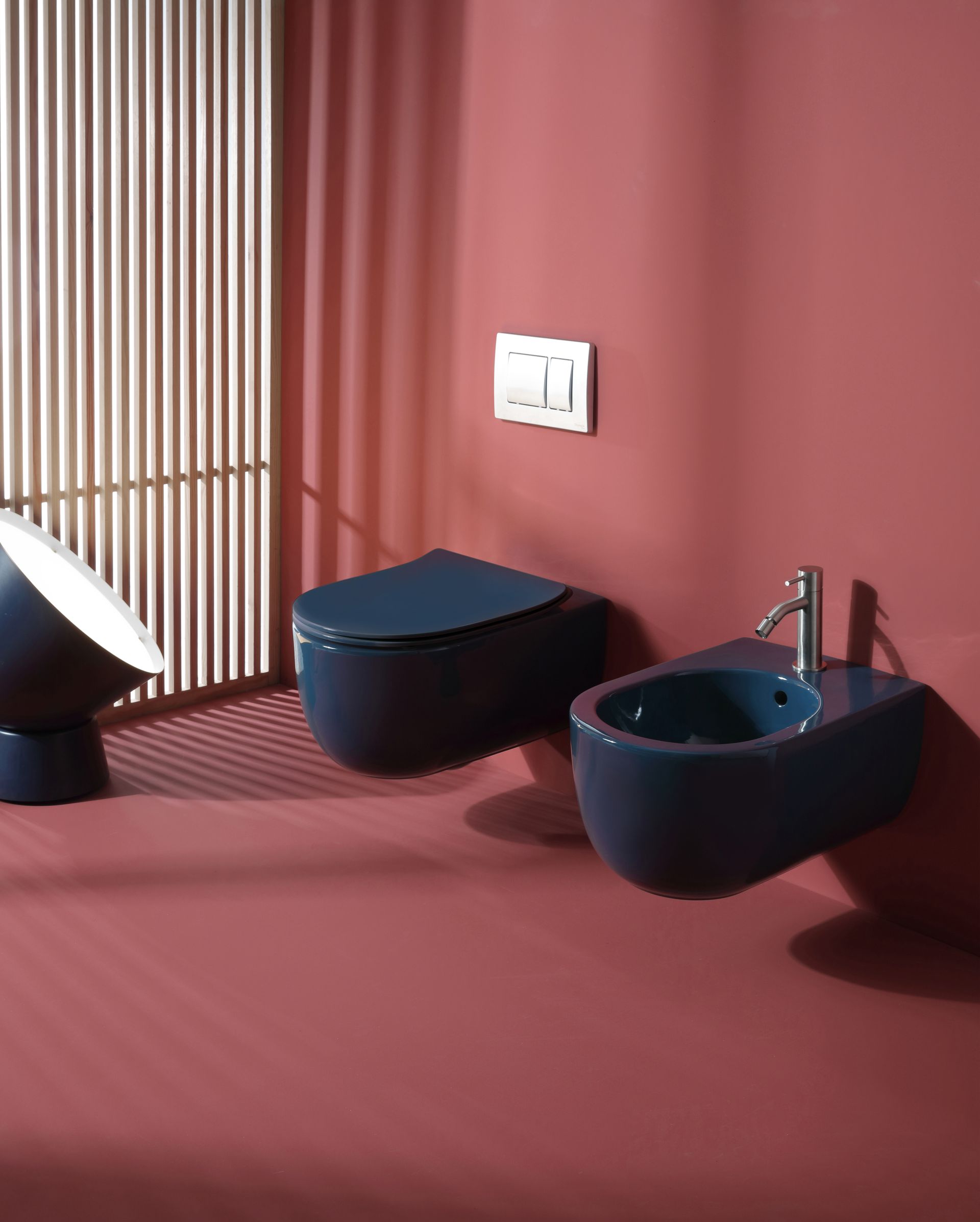 WC, bidet e lavandino blu contro una parete rosa con finestra a doghe.