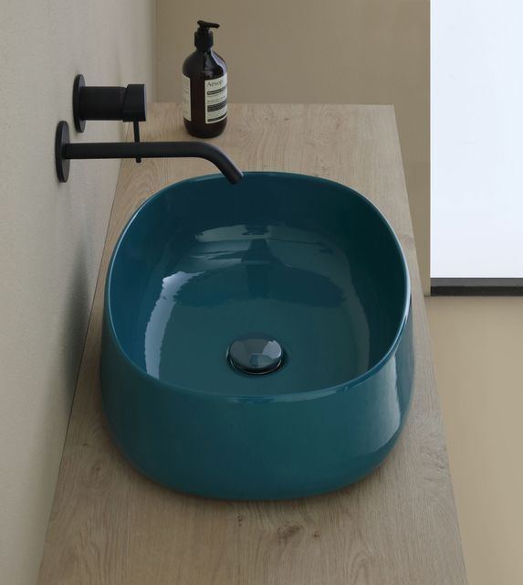 Lavandino color verde acqua su ripiano in legno con rubinetto nero e flacone di sapone.